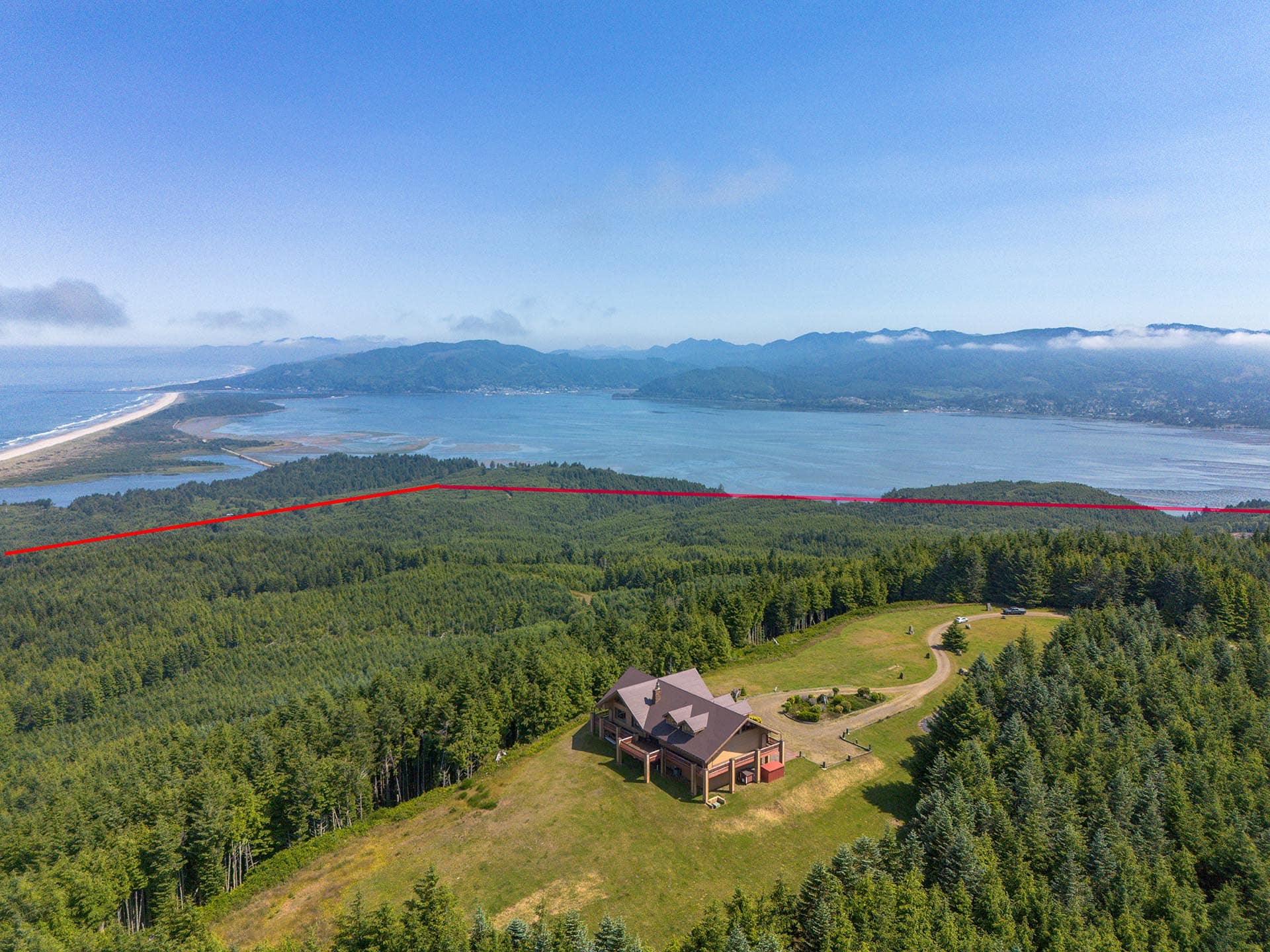 Aerial view of a forested hillside with a large house and curved driveway; a red boundary line crosses the foreground slope.