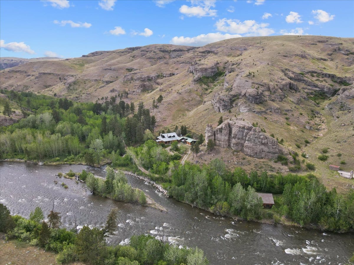 A riverside valley with dense trees, a winding river, and a cluster of cabins at the base of rocky hills.