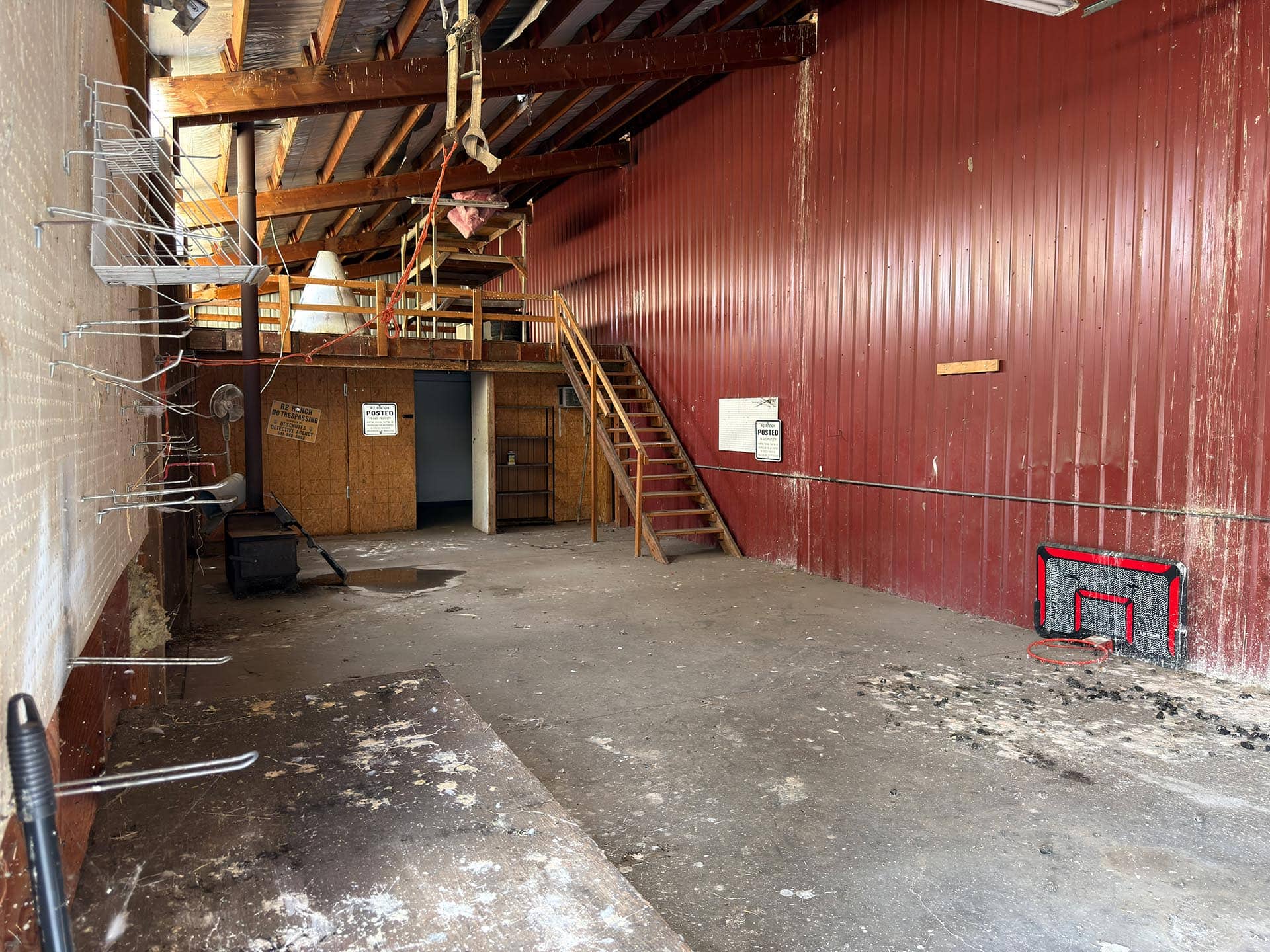 Interior of an abandoned industrial space with red corrugated metal wall, wooden stairs, and cluttered upper platform.