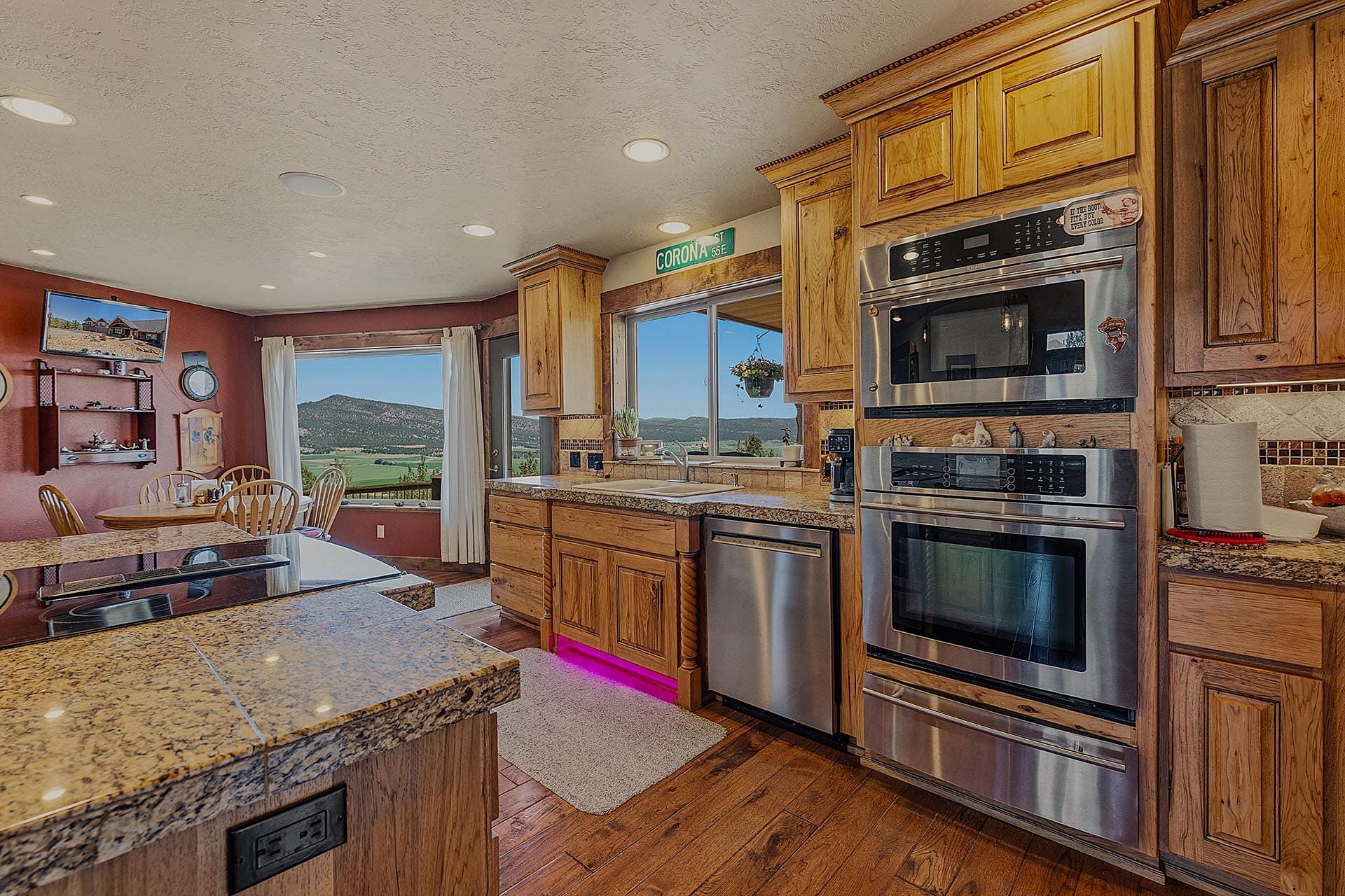 Bright kitchen with granite countertops, maple cabinets, and a stainless steel double-oven setup; large window shows hills outside.