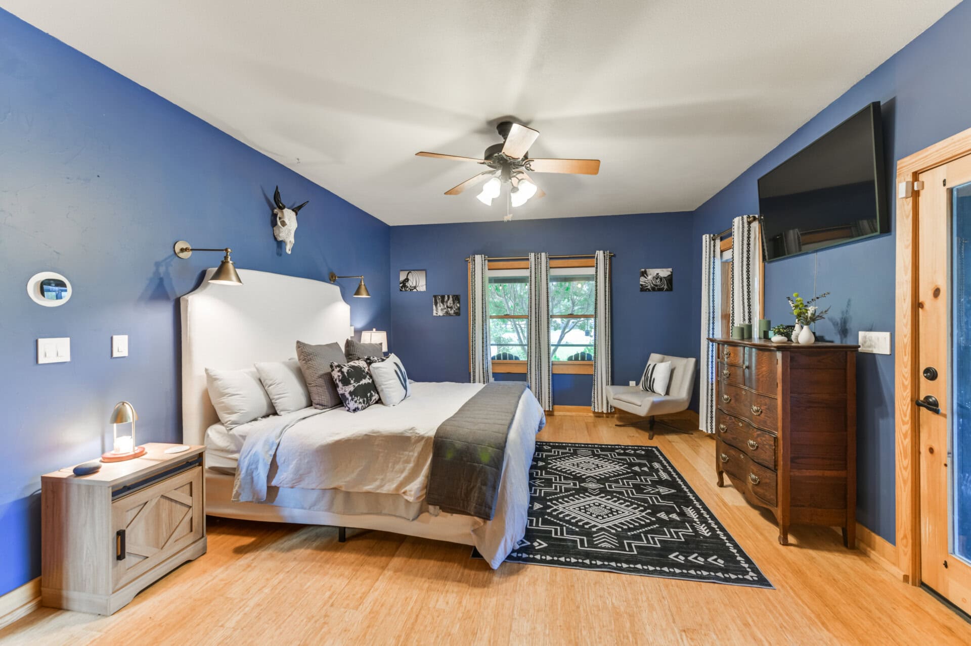 Blue bedroom with a white upholstered bed, multiple pillows, and wooden nightstands under a ceiling fan