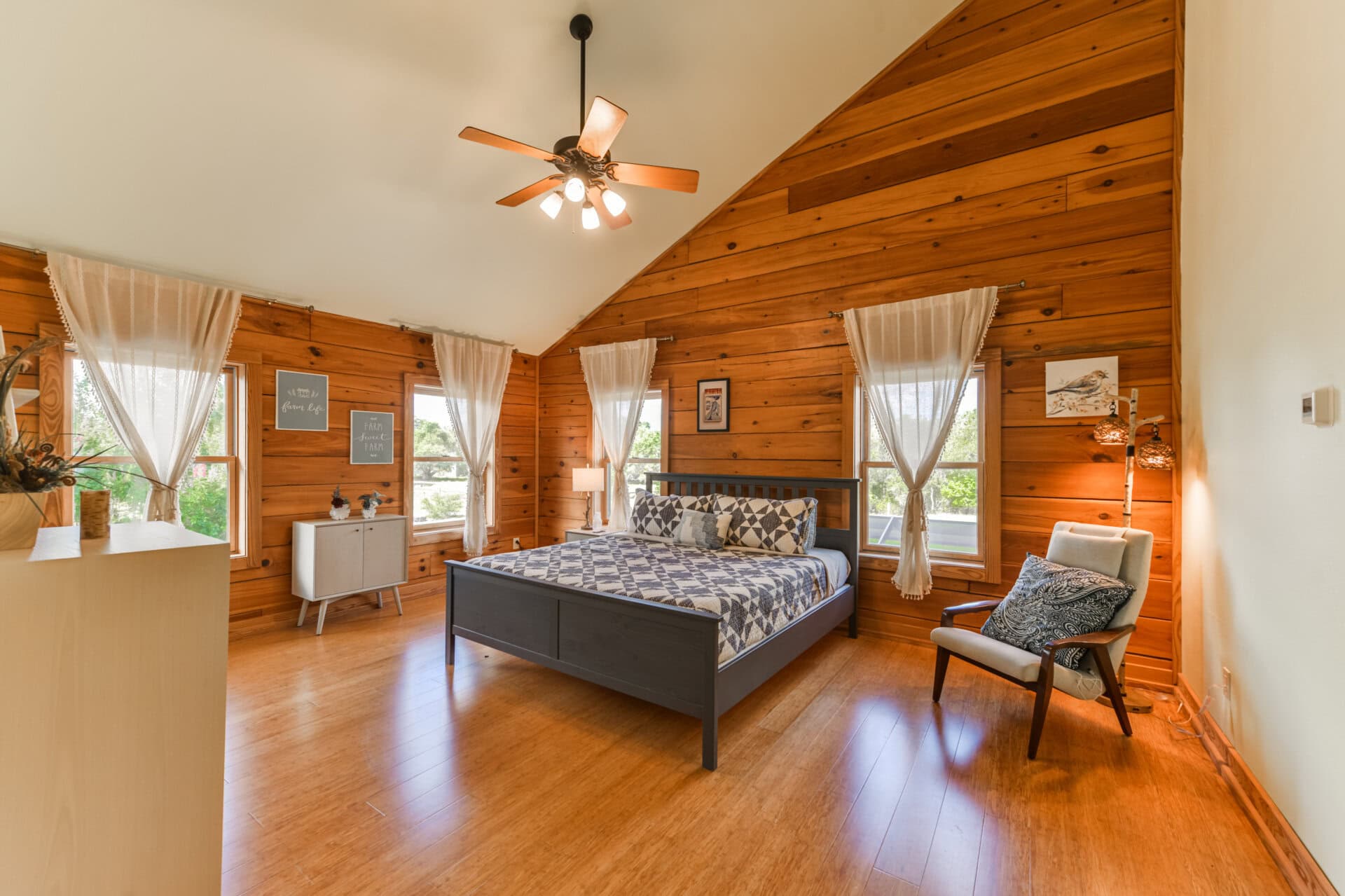 Cozy rustic bedroom with wooden paneling, large bed, and ceiling fan under a sloped ceiling.