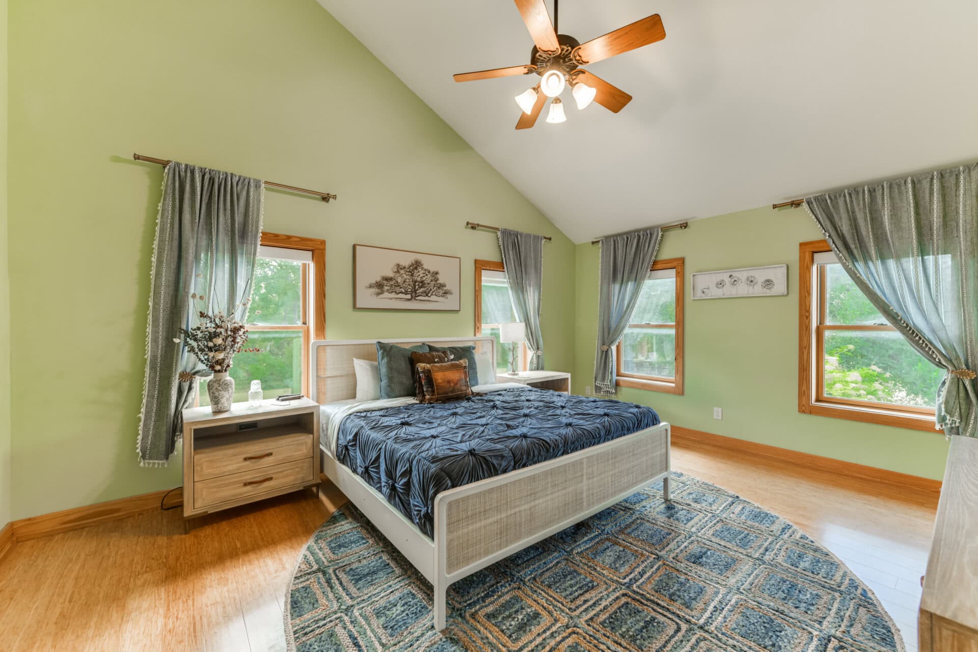 Cozy bedroom with green walls, a white bed, and blue patterned rug under a ceiling fan with wooden blades.
