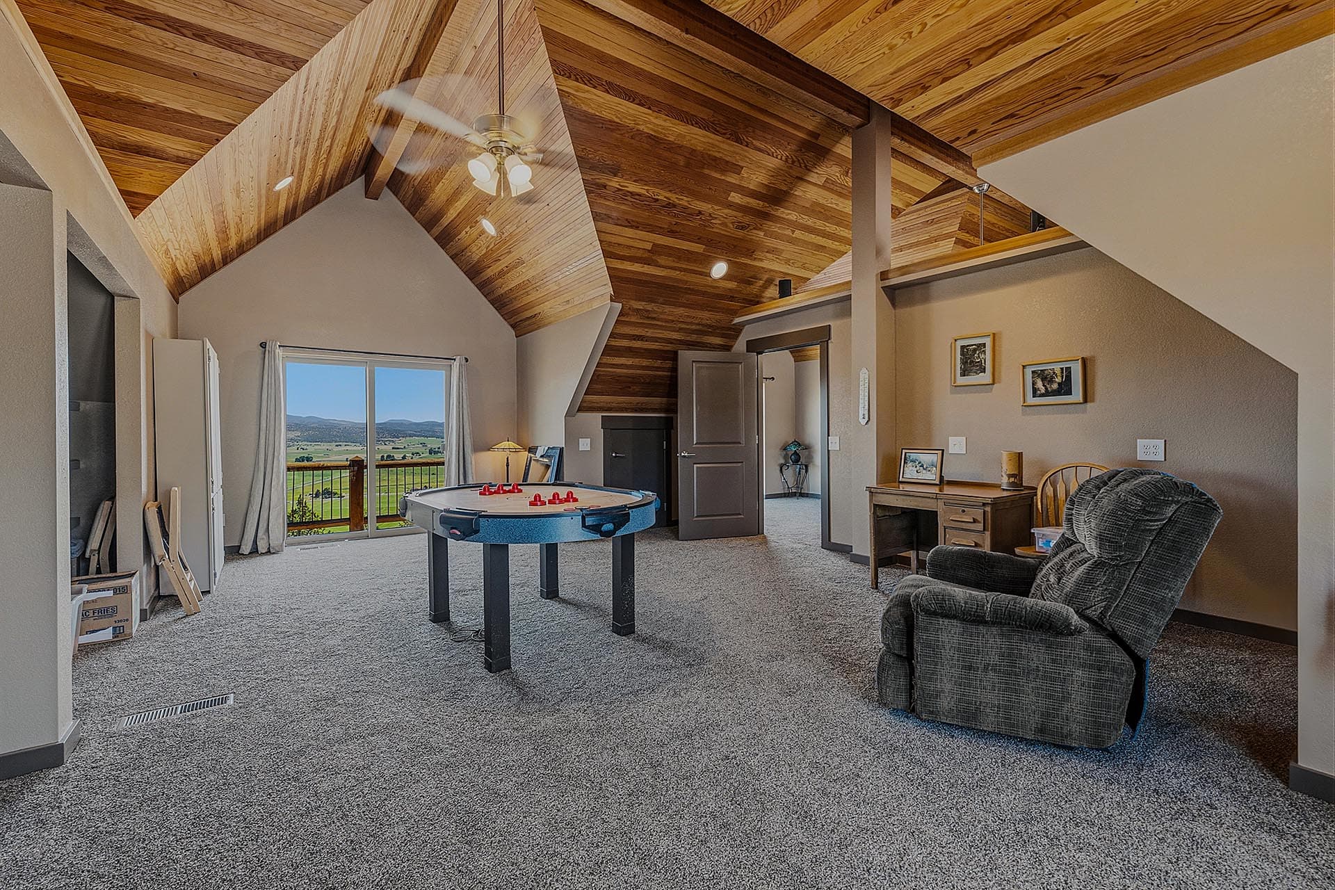 Attic recreation room with a foosball table, seating, and a balcony door opening to a rural landscape.