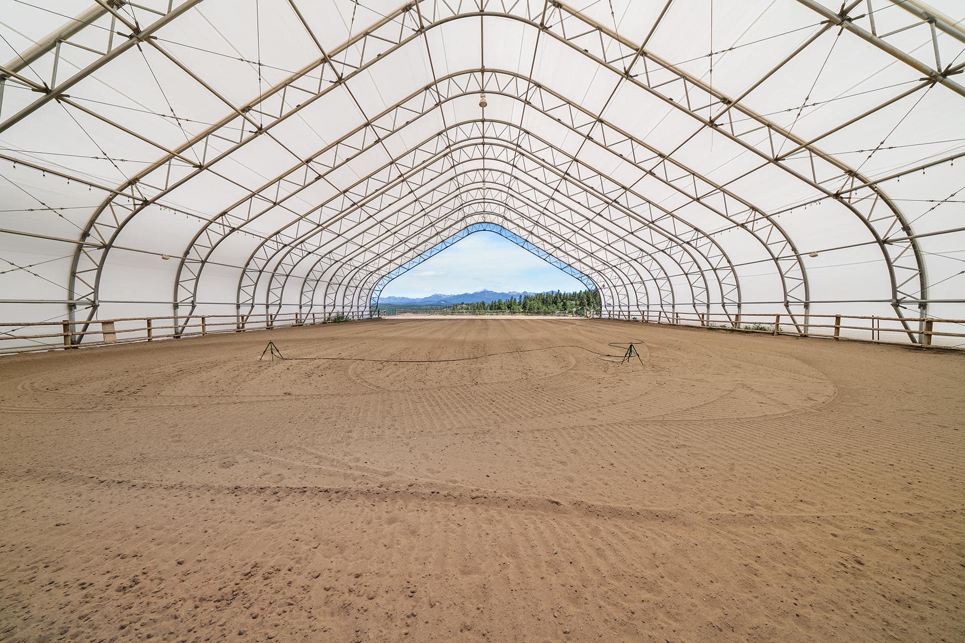 A long arched greenhouse frame with white cover, leading to a distant mountain landscape through the open end.