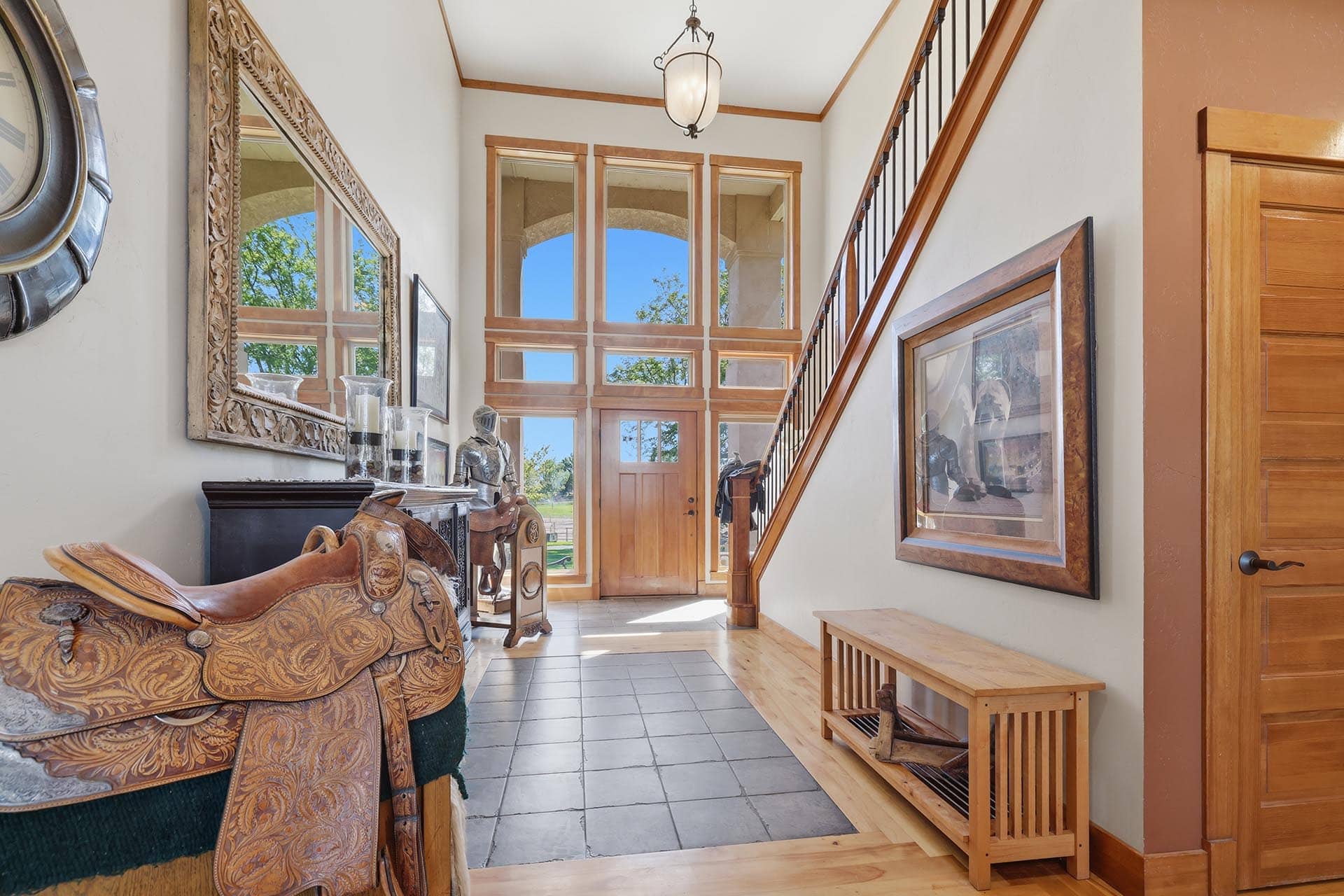 Elegant foyer with ornate mirror, wooden stair rail, and large grid of windows letting in bright outdoor light