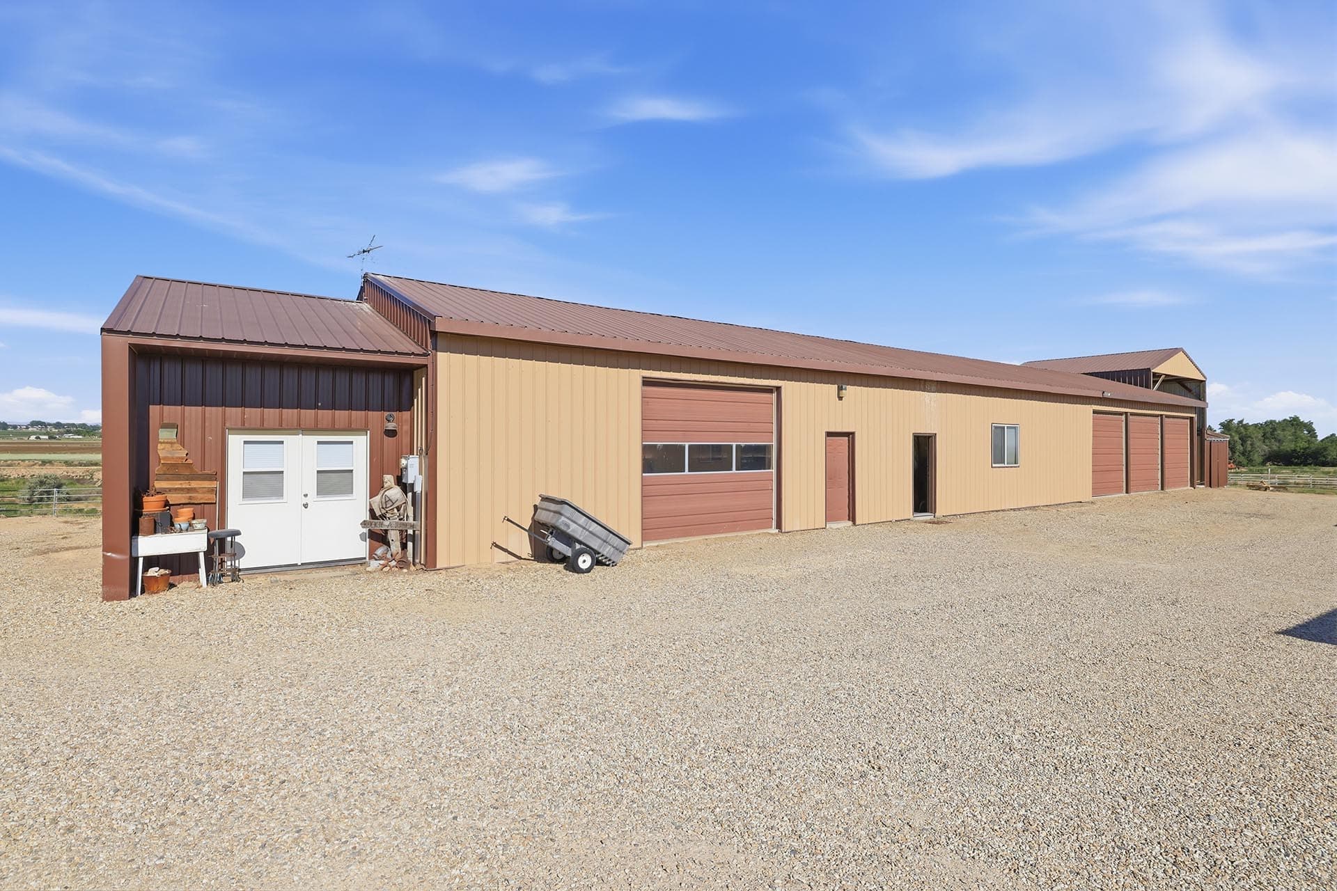 Long beige and brown metal warehouse with multiple bays on a gravel lot under a clear blue sky