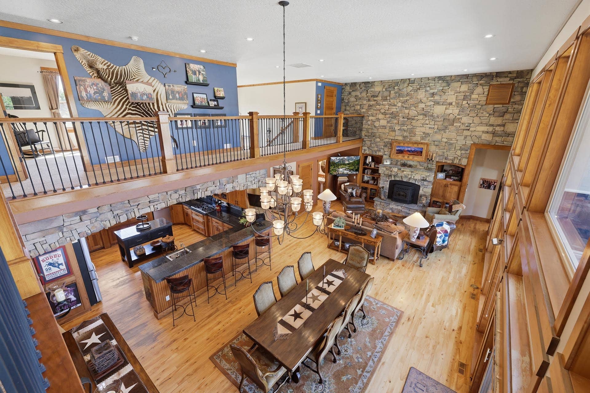 Open living space with a stone fireplace, mezzanine railing, blue wall featuring a zebra mural, and a long dining table with chairs.