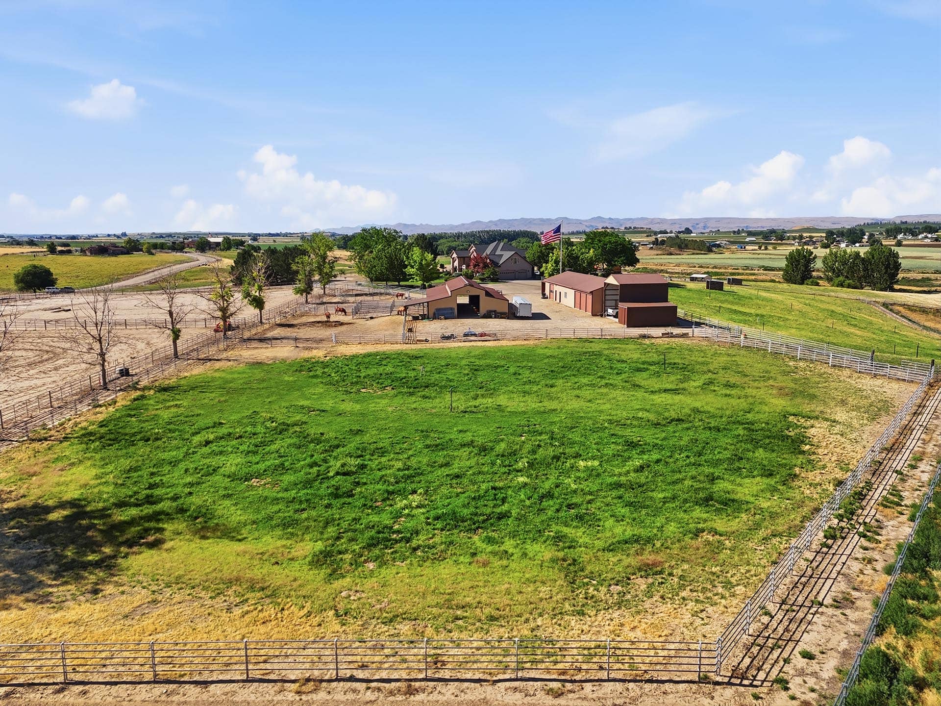 Rural farmyard with barns, fences, and an American flag under a bright blue sky.