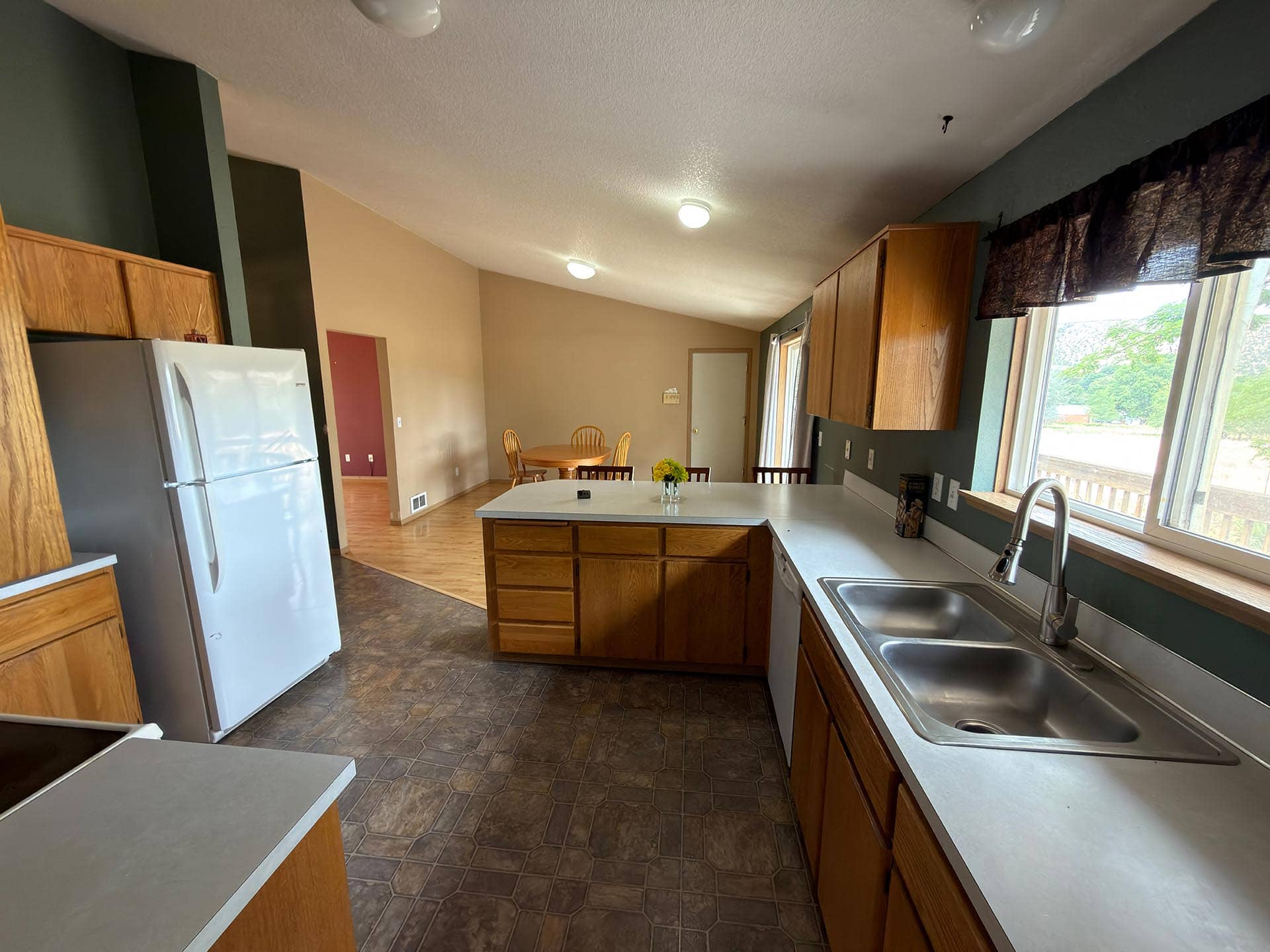 Kitchen with an island, wooden cabinets, and a double sink; dining table visible in the back.