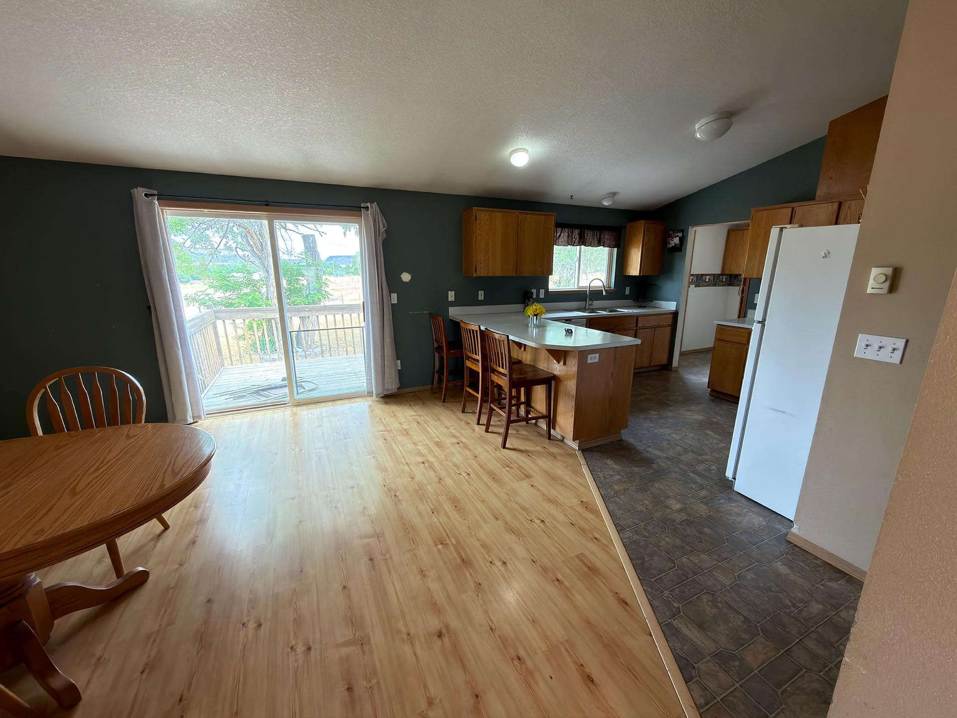 Open kitchen and dining area with wood cabinets, an island with three stools, and a sliding glass door to a deck outside.