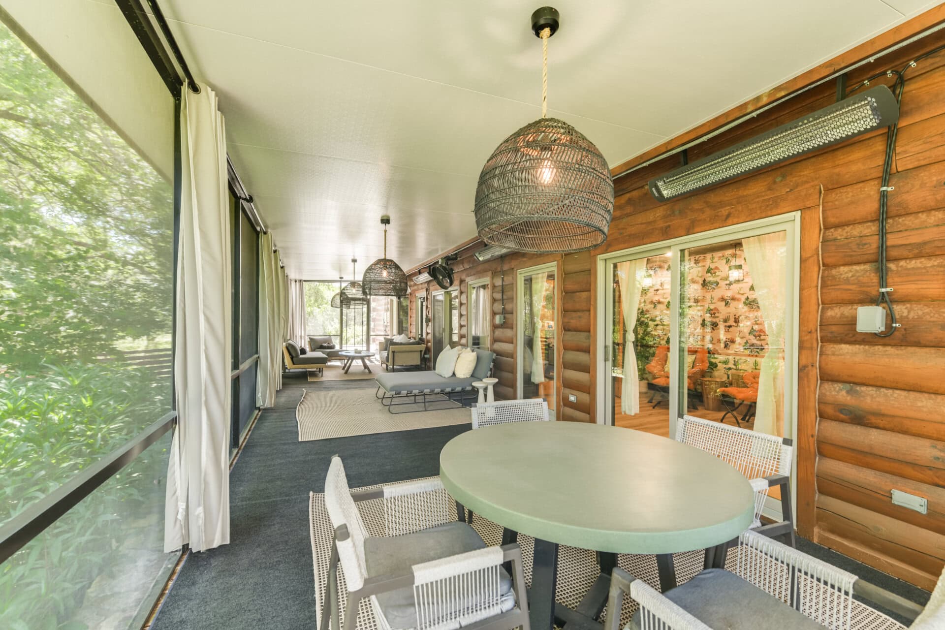 Covered cabin porch with wicker pendant lights, green round table, and white woven chairs along a seating area.