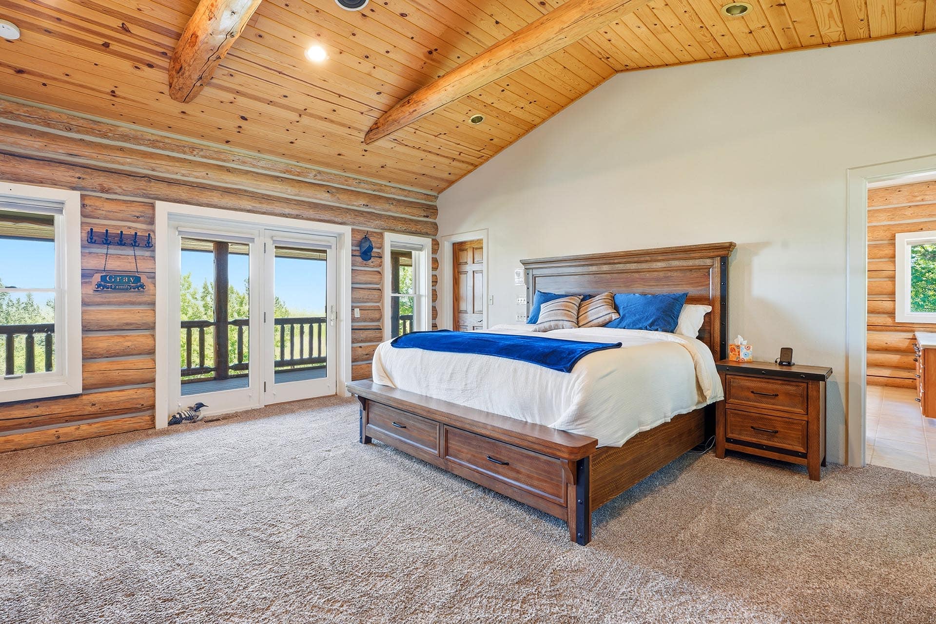 Cozy log-cabin bedroom with a wooden bed, blue pillows, and glass doors to a deck.