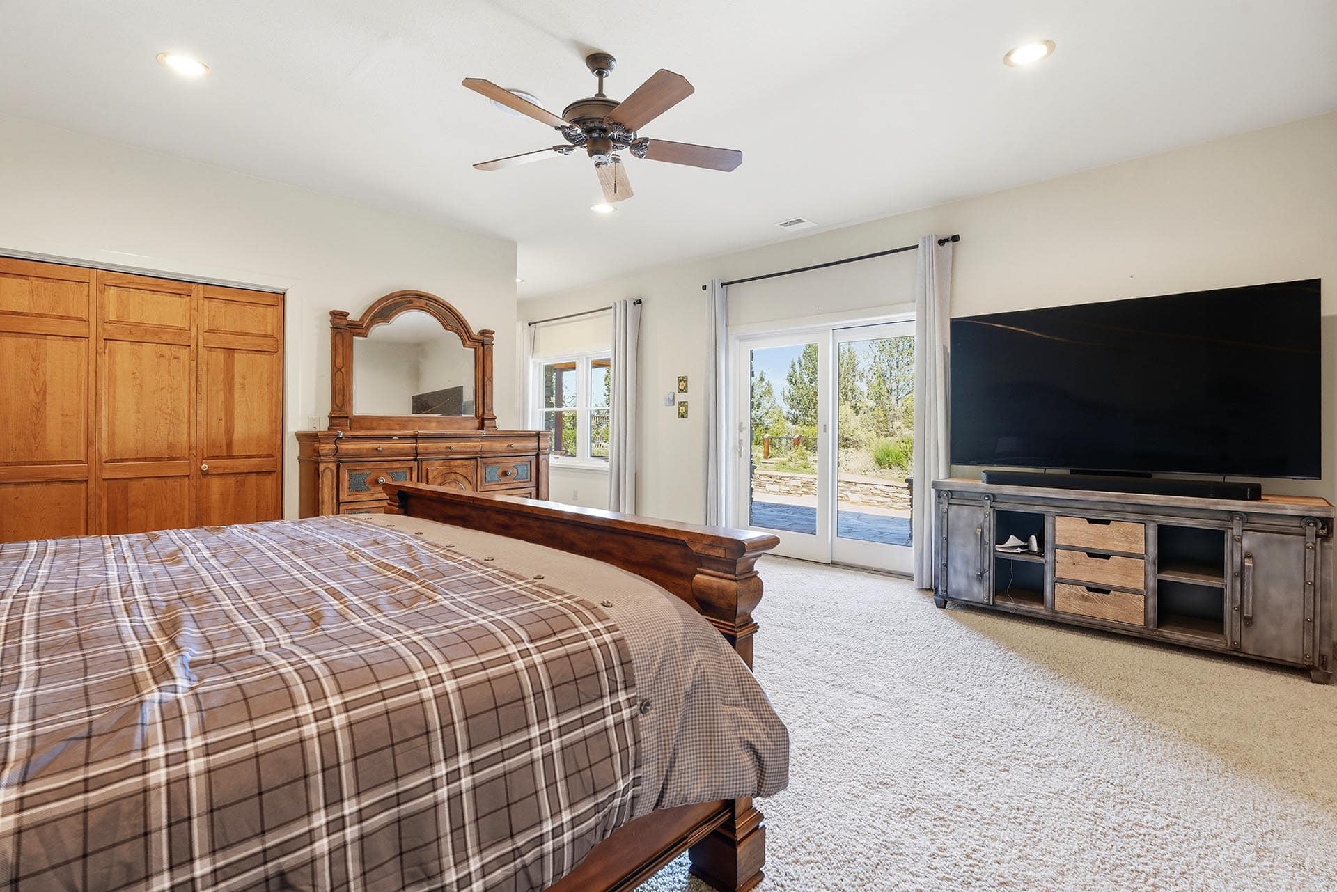 Bedroom with a wooden bed, matching dresser and arched mirror, and a large TV on a gray console facing the room.