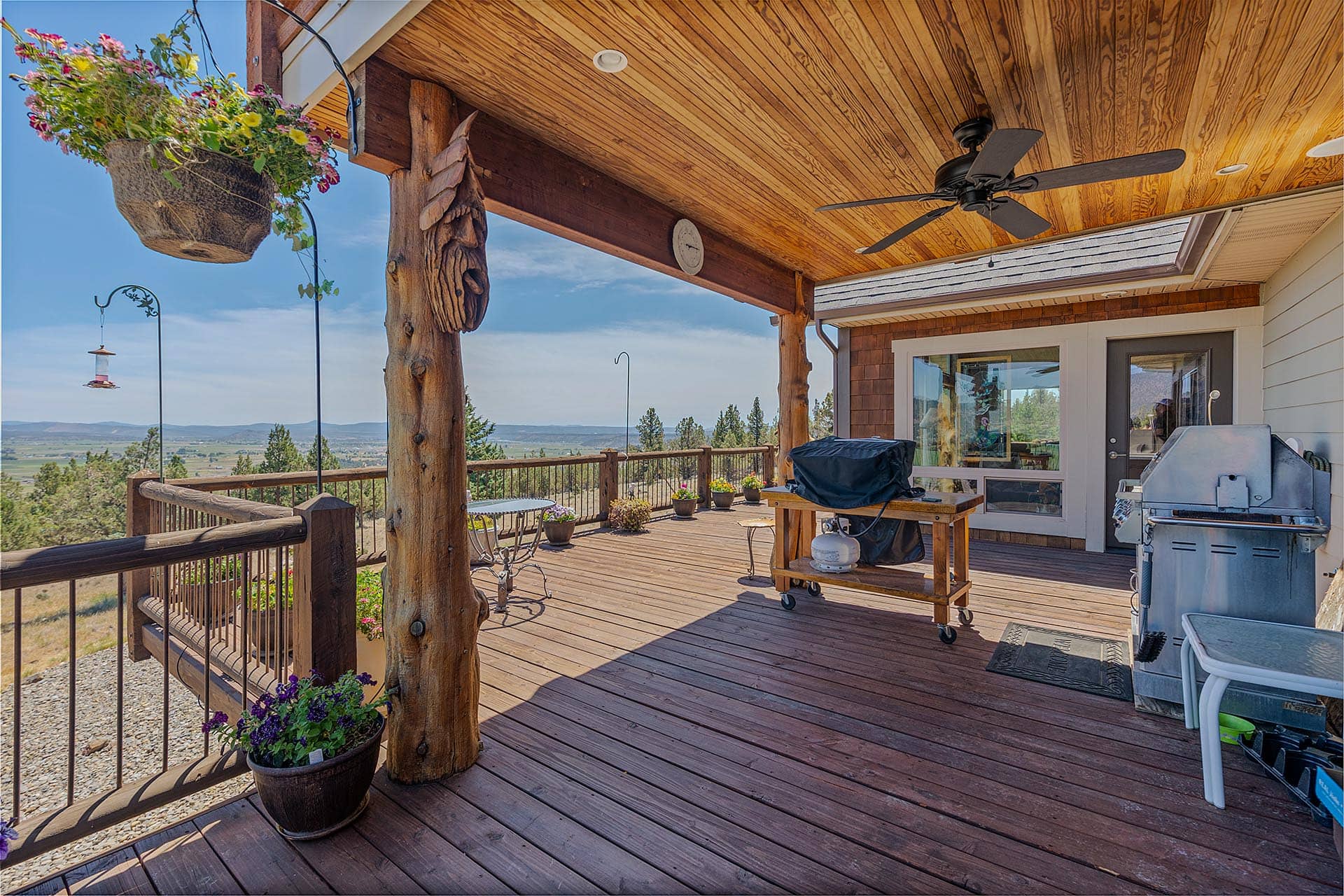 Wood deck patio with hanging flower basket, log porch posts, and mountains in the distance.