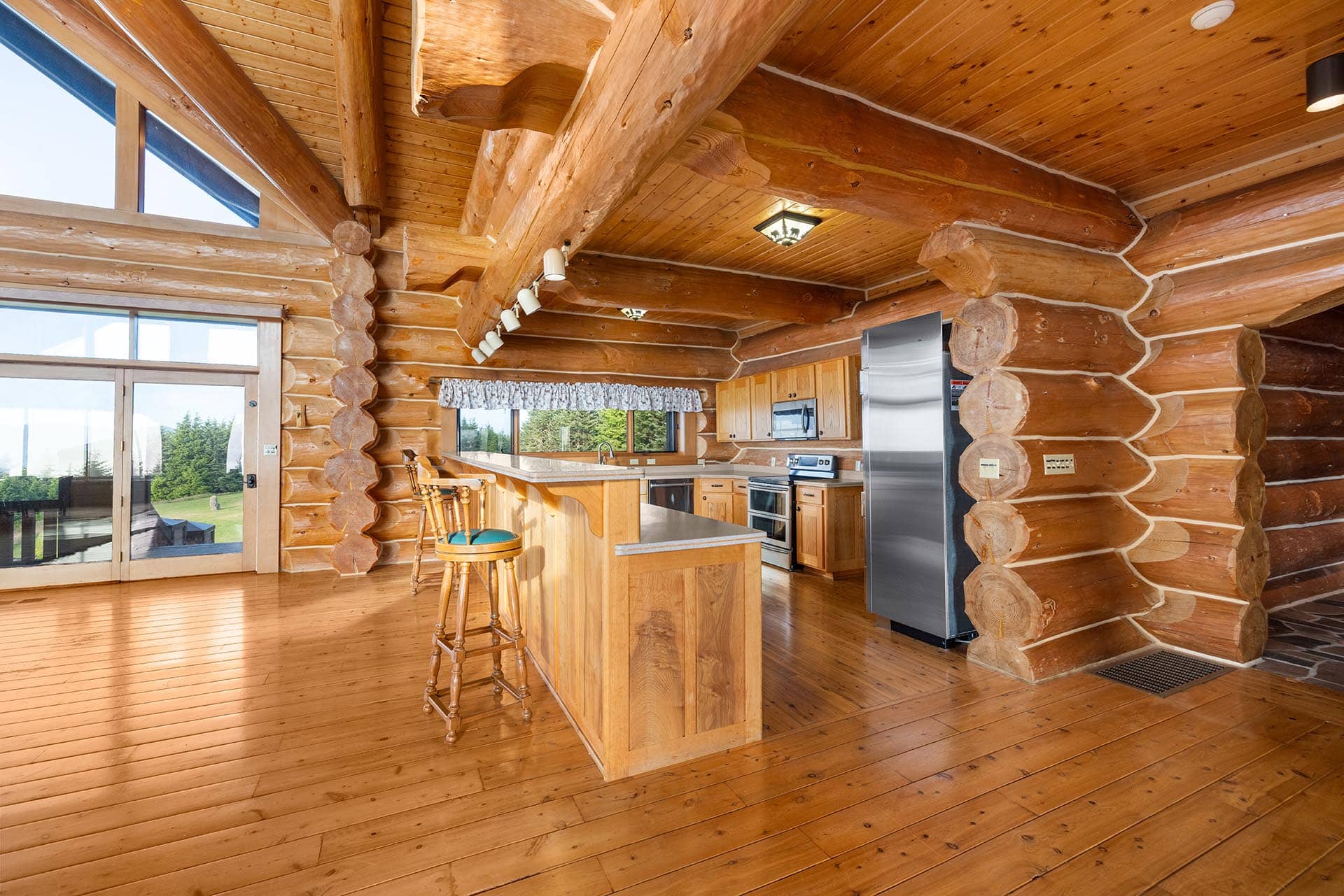 Open-concept log cabin kitchen with a large wooden island, beams, and stainless steel appliances.