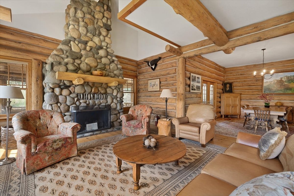 Cozy rustic living room with a towering stone fireplace, heavy wooden beams and comfortable seating.