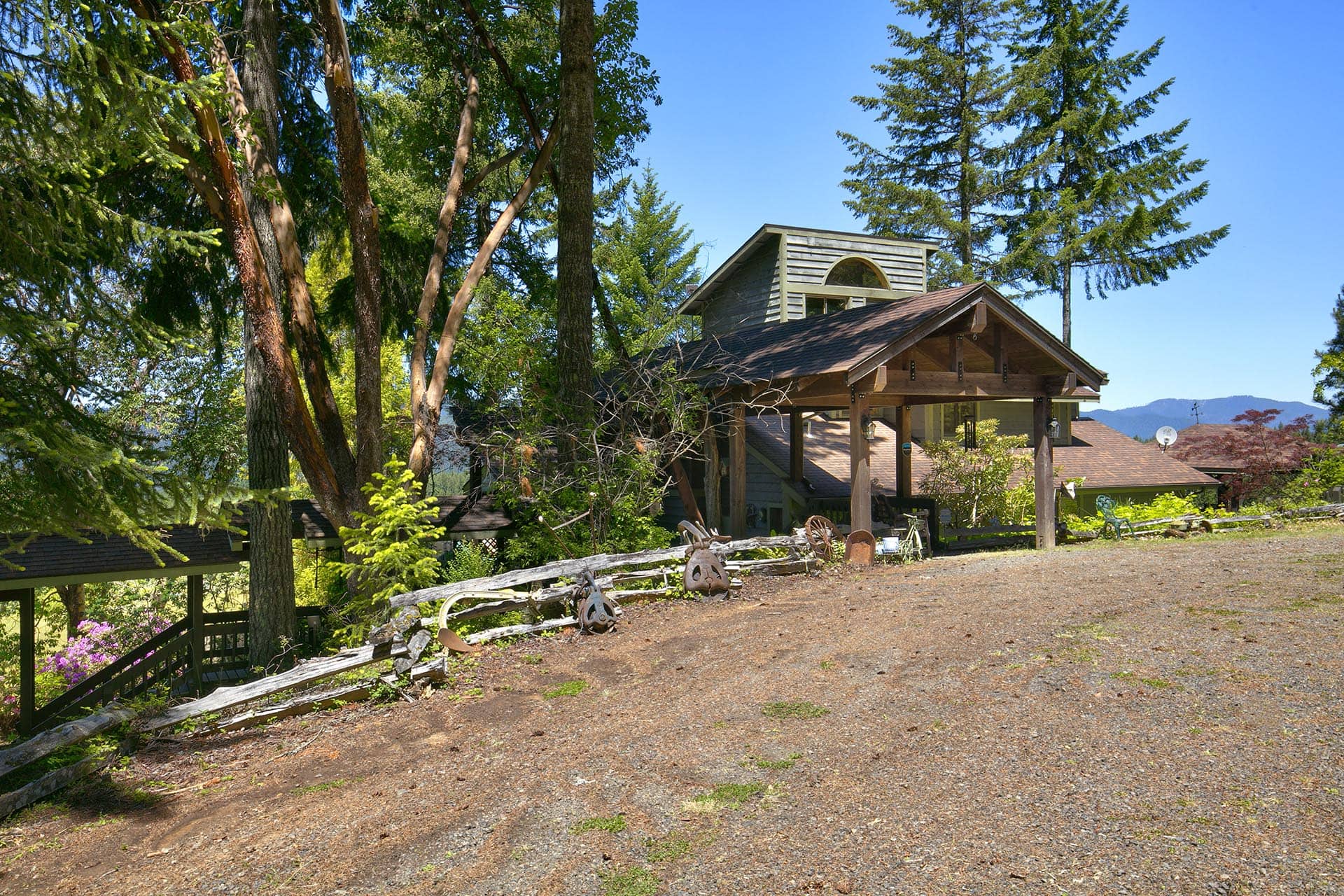 Rustic wooden house with a covered porch tucked among tall evergreen trees under a clear blue sky.