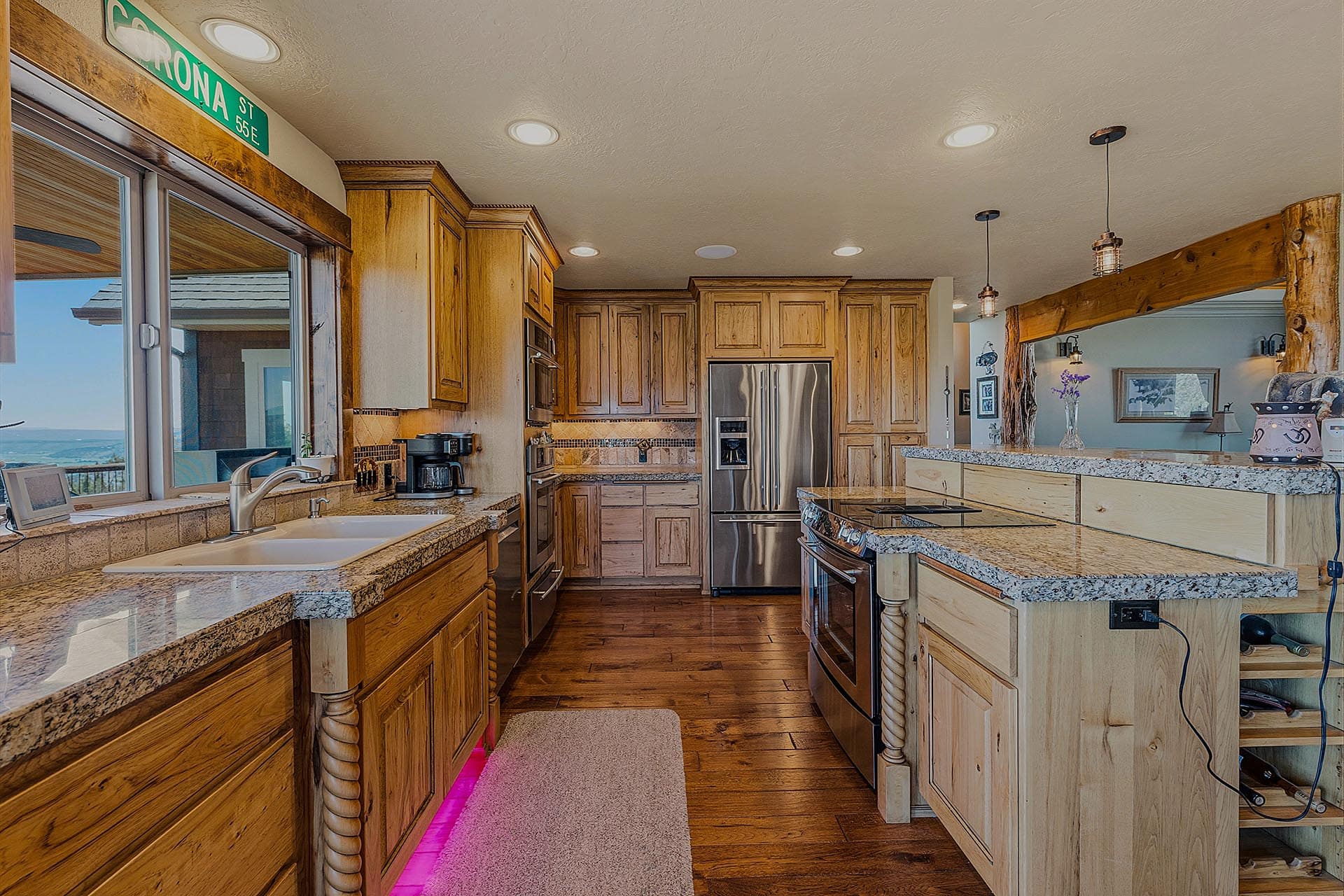Spacious rustic kitchen with wooden cabinets, granite countertops, island, and stainless steel fridge, overlooking an ocean view through large windows.