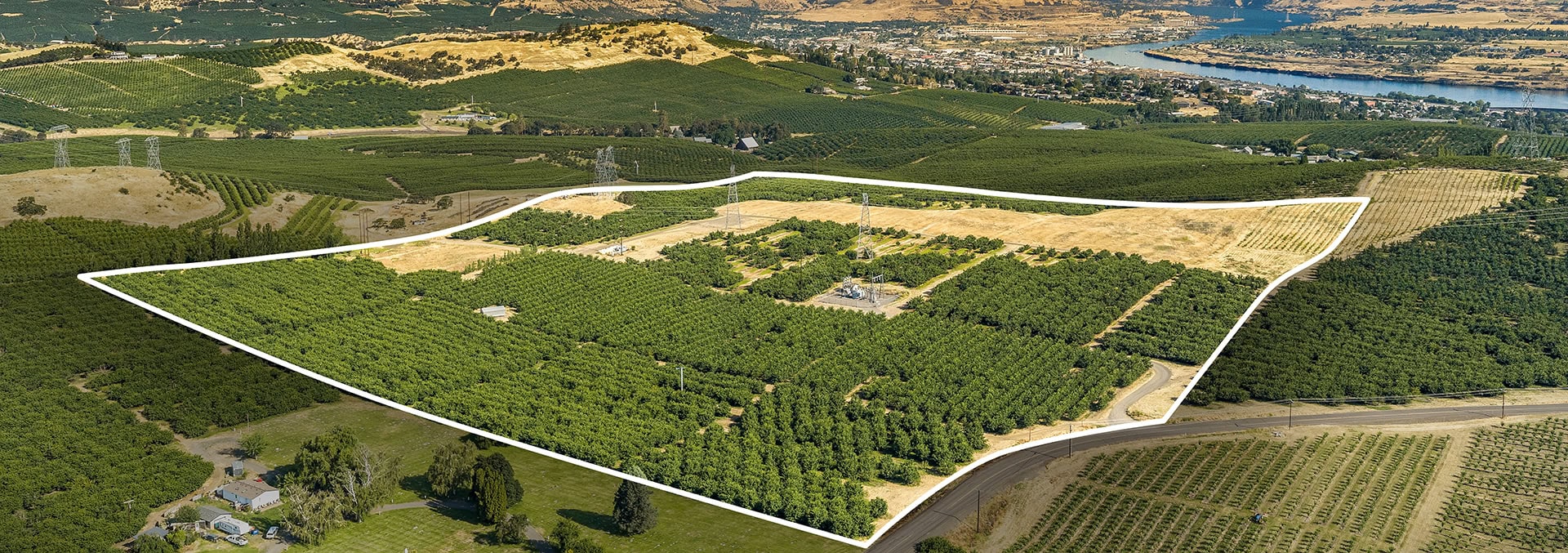 Aerial view of a large rural parcel outlined in white, showing orchards, power lines, and surrounding fields with a nearby road network.