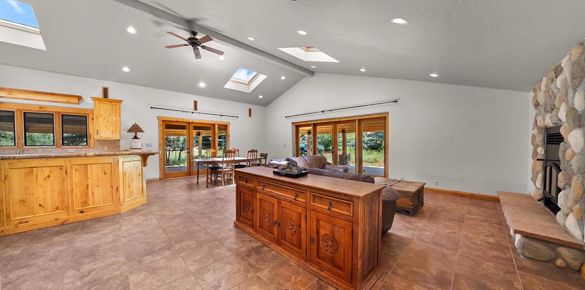 Open-concept living room with wood cabinetry along the kitchen bar, a central wooden sideboard, leather seating, and glass doors to the yard.
