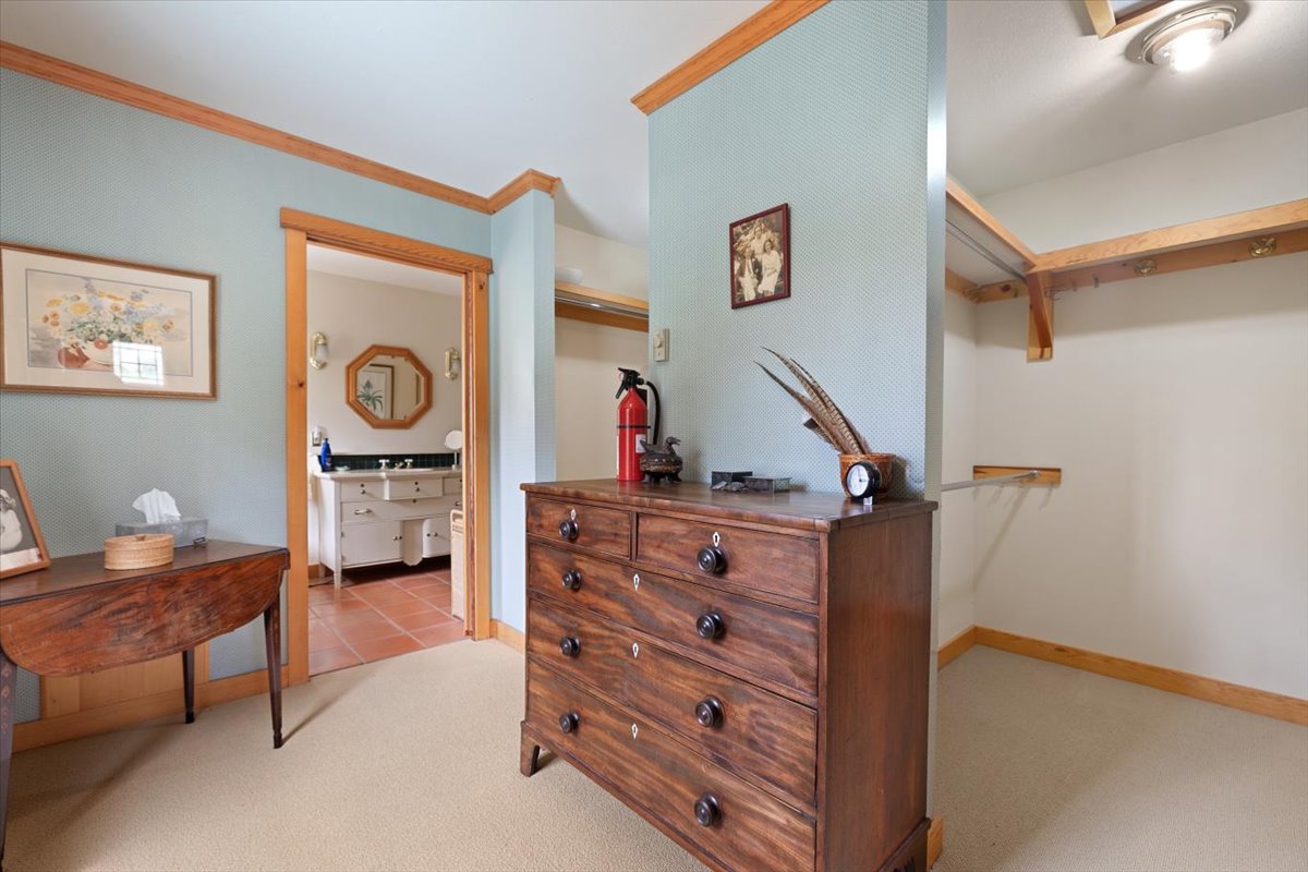 Antique wooden dresser in a blue-walled bedroom with a fire extinguisher and clock on top; open closet and doorway to a bathroom in the background.