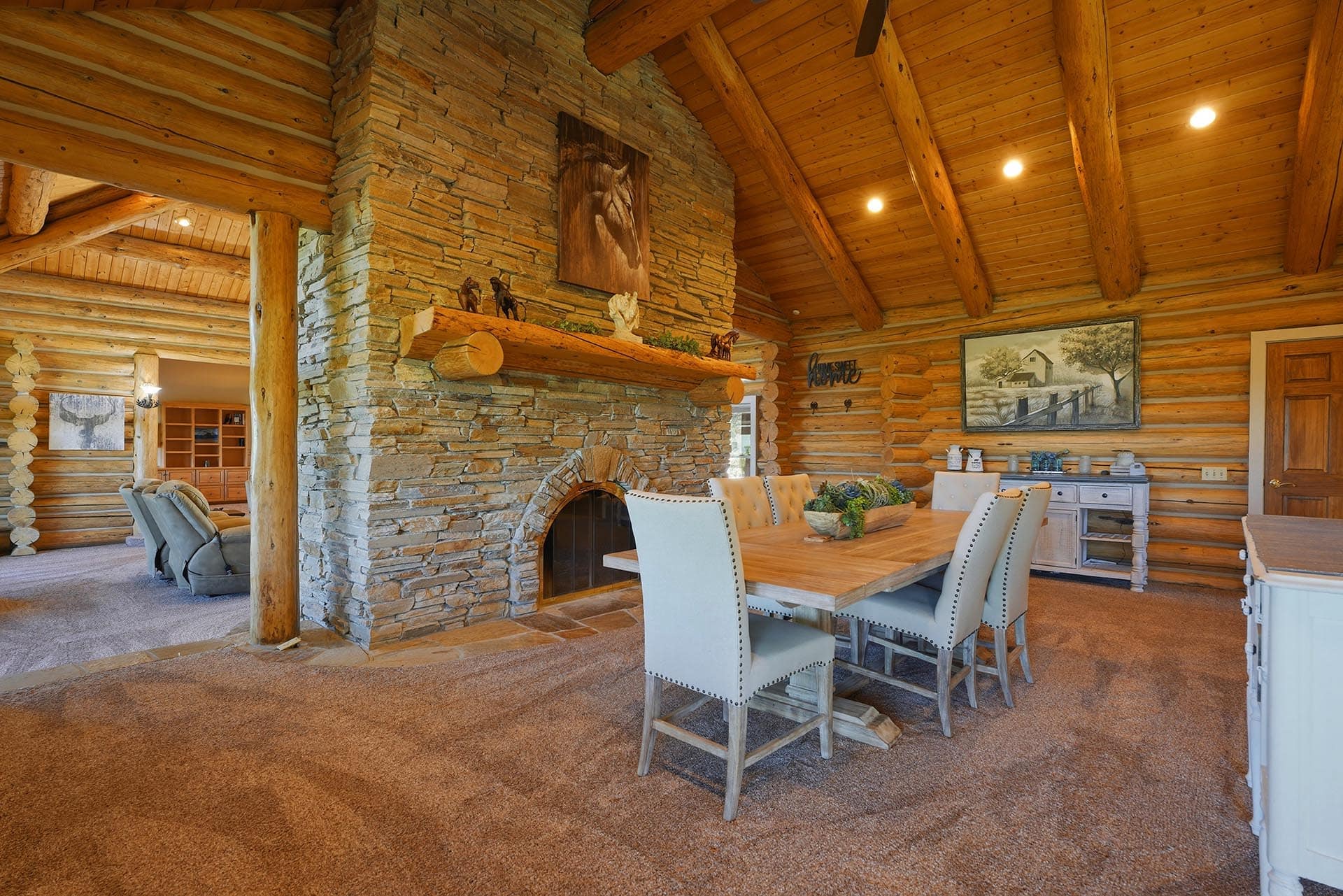 Rustic log cabin dining area with a stone fireplace and vaulted wooden beam ceiling.