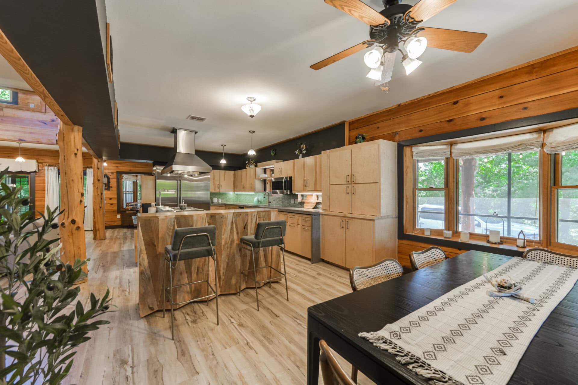 Open-concept kitchen with wooden beams, island bar, stainless steel range hood, and large windows letting in natural light.