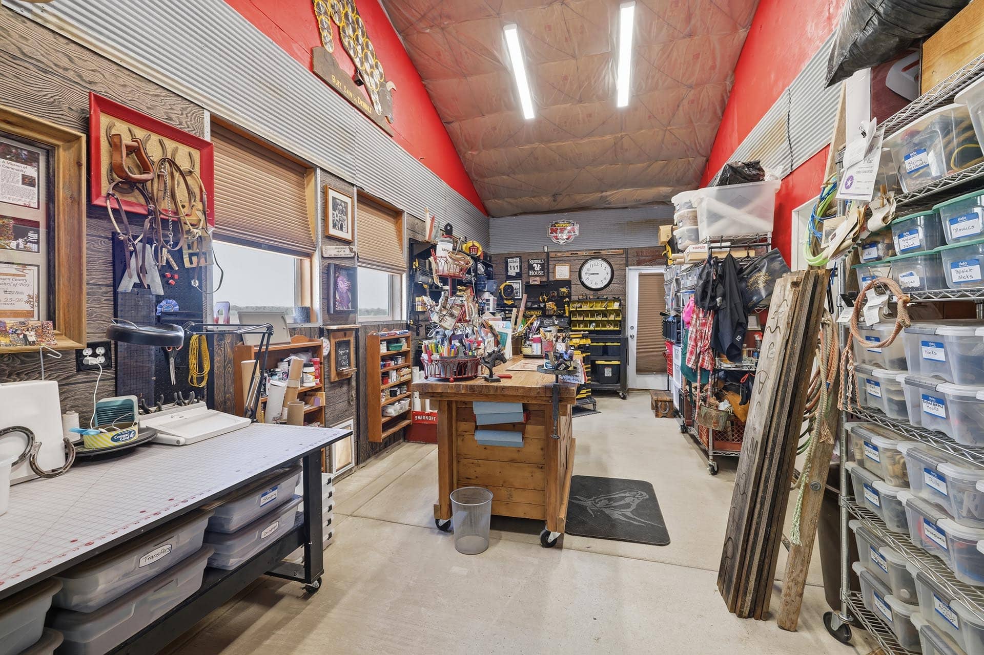 Busy workshop filled with tools, pegboards, and a central worktable on wheels in a cluttered shop space.