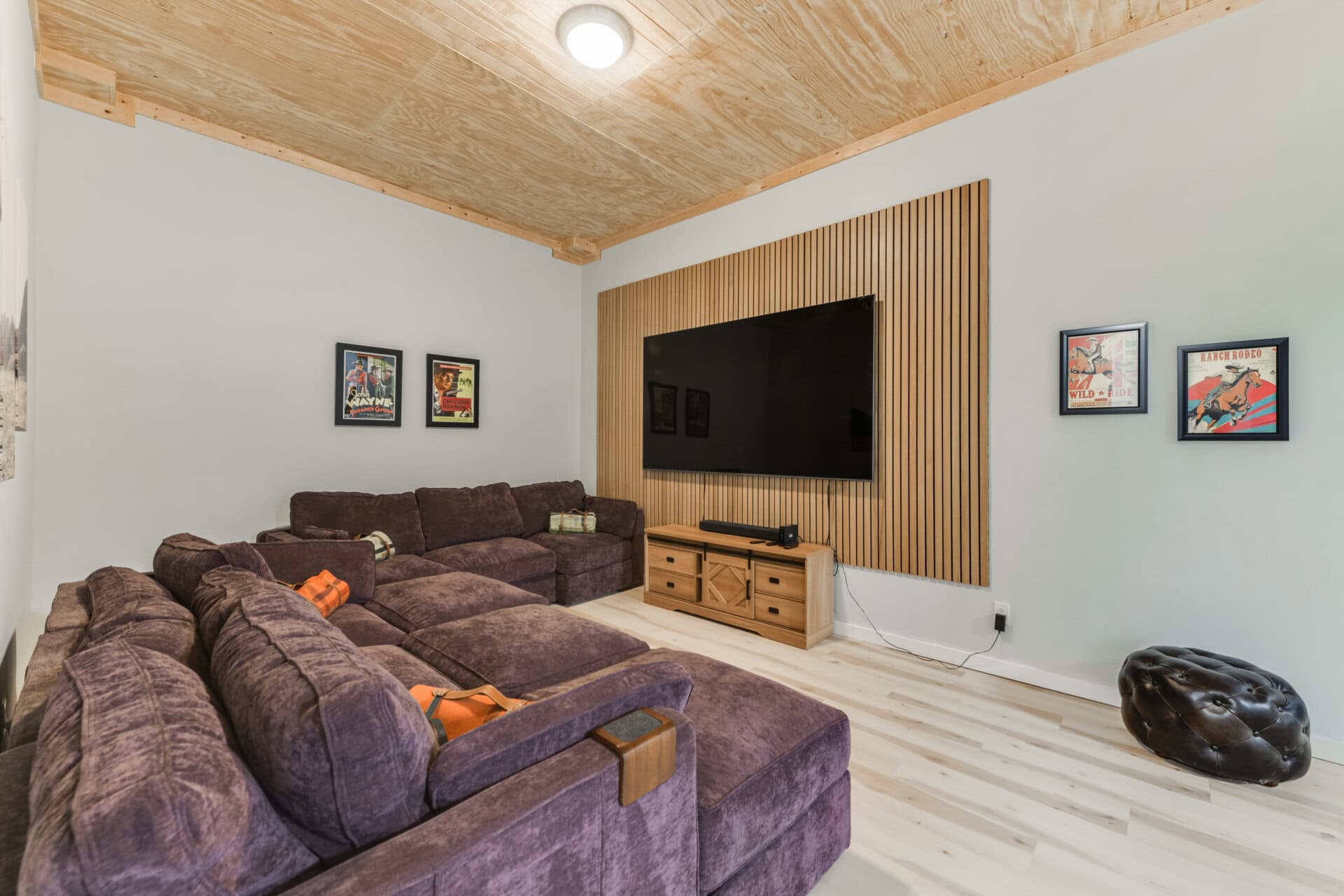Cozy living room with a large purple sectional sofa, light wood floors, and a wall-mounted TV on a wood slat backdrop.