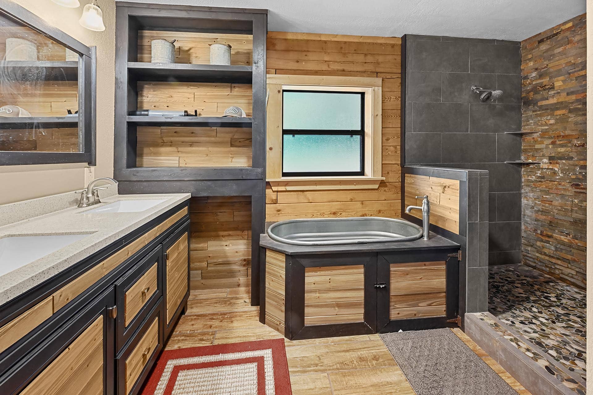 Rustic bathroom with black-framed, wood-paneled cabinetry, dual sinks, and a freestanding tub beside a frosted window.