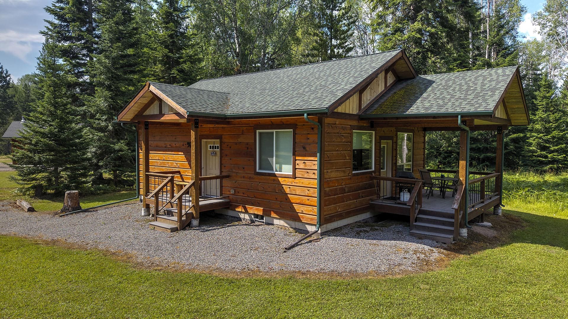 Wooden cabin with a covered porch and outdoor seating in a forest clearing.