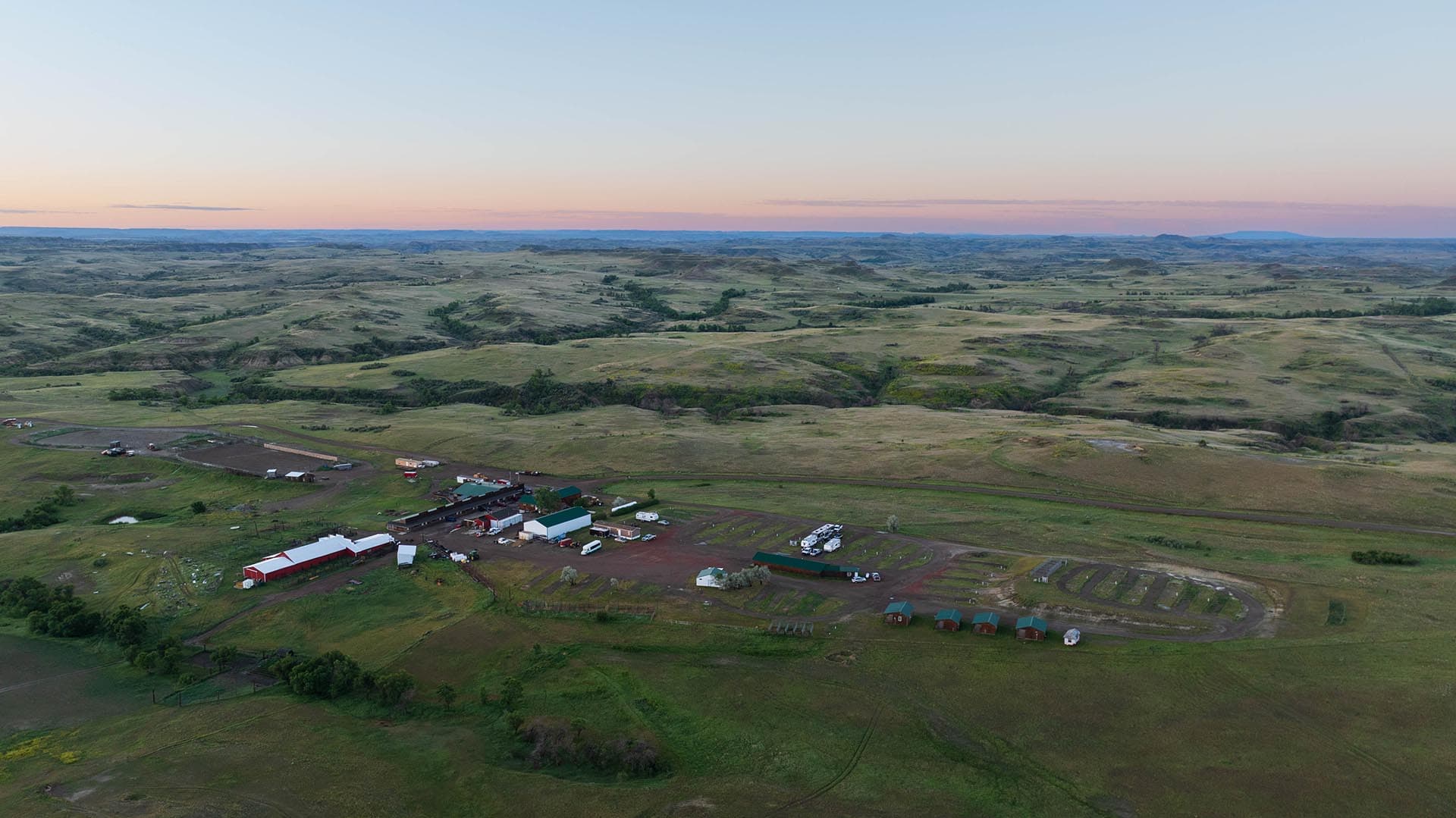 Aerial view of a rural valley with rolling green hills and a farm complex in the foreground at dusk.