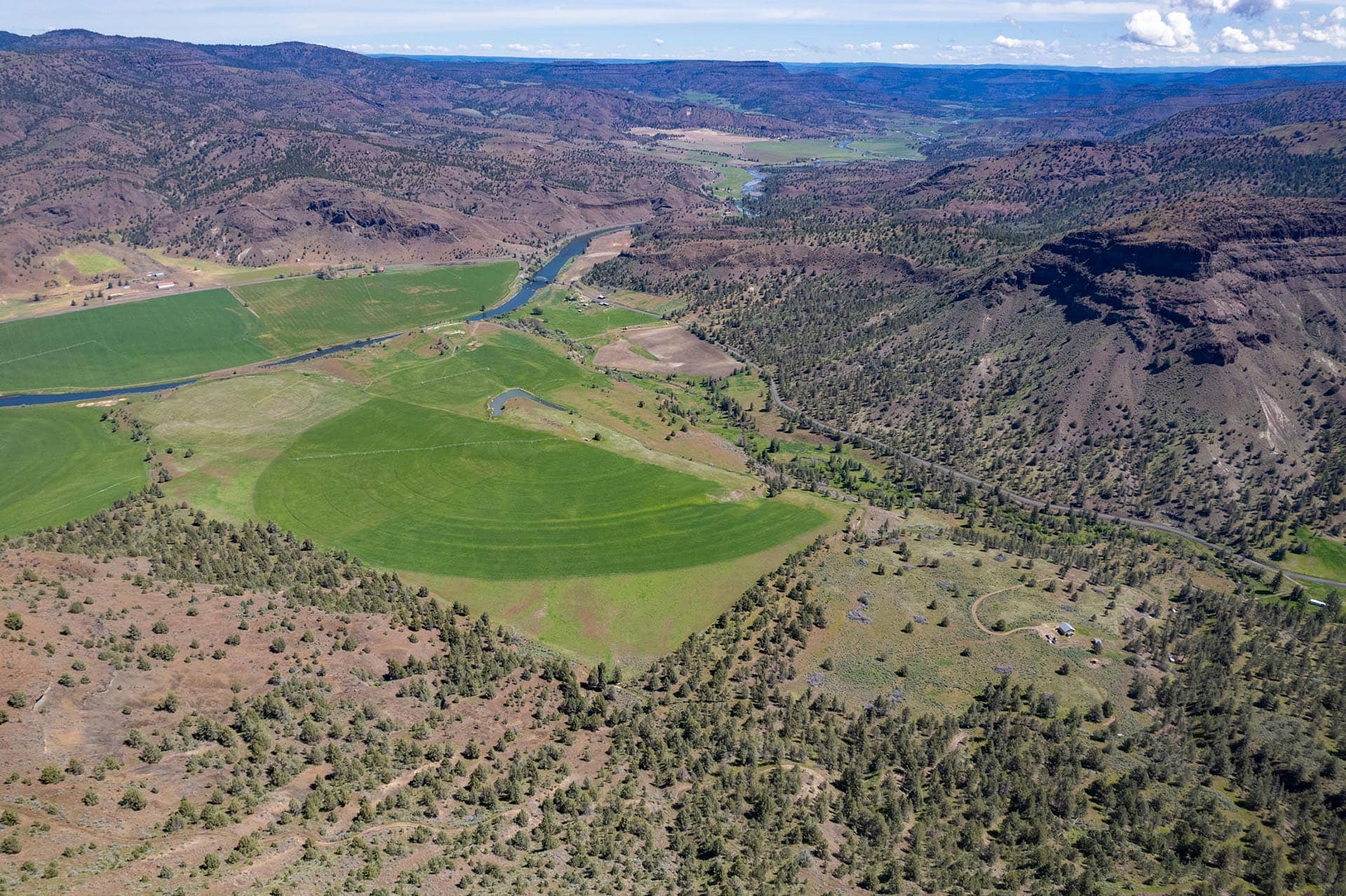 Aerial view of a winding river through green farmland and brown hills in a valley.