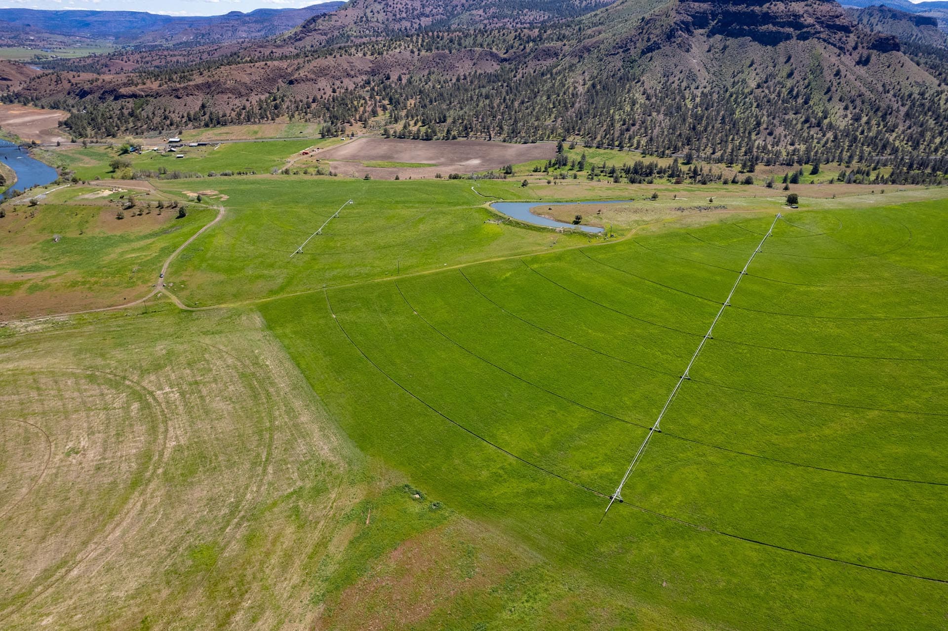 Aerial view of green farmland with power lines crossing the fields, hills in the distance and a river to the left.