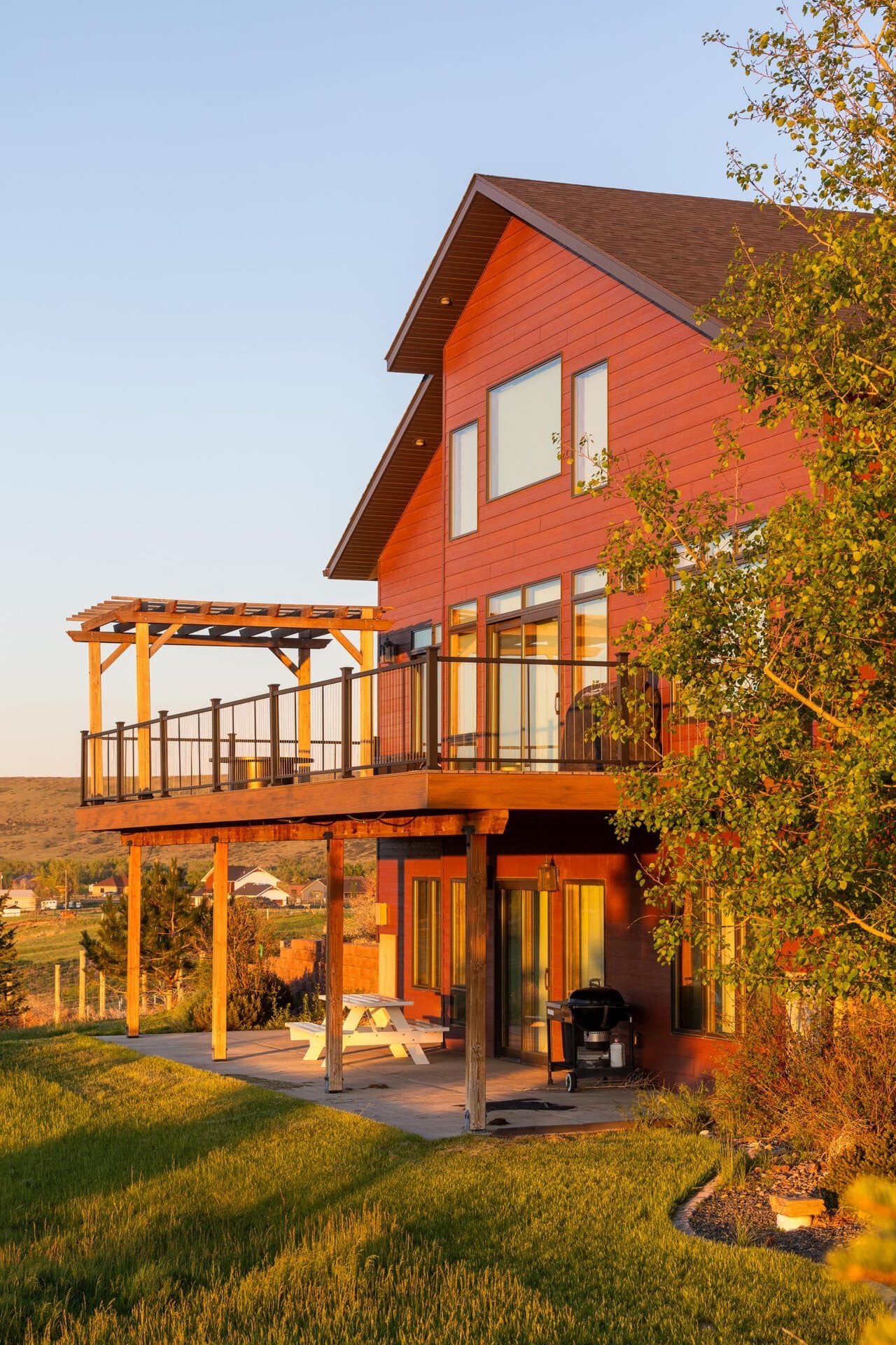 Red two-story house with a large wooden deck and railing, bathed in golden sunset light.