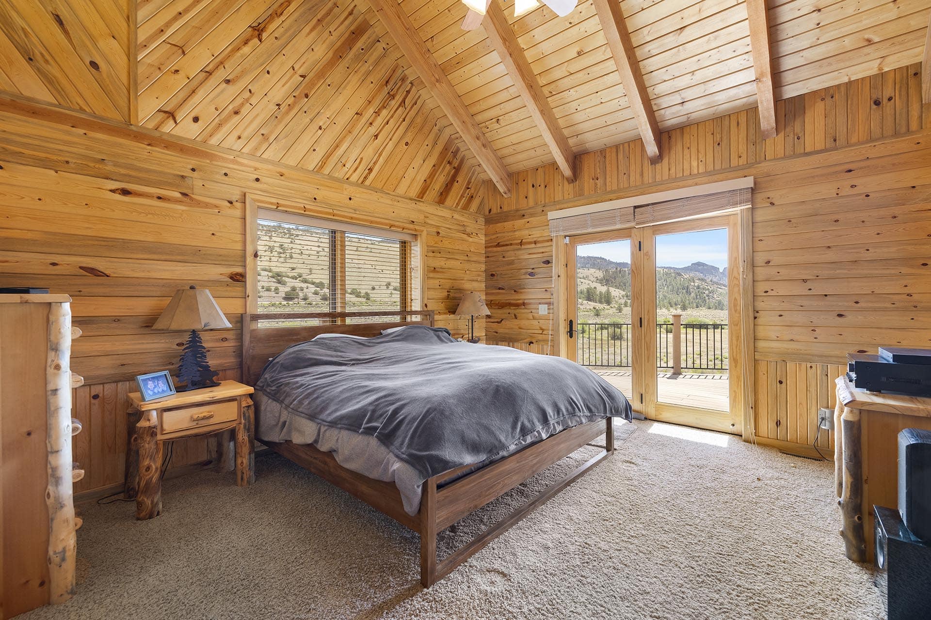 Rustic wooden bedroom with a large bed, log walls and a deck door opening to a mountain view outside.