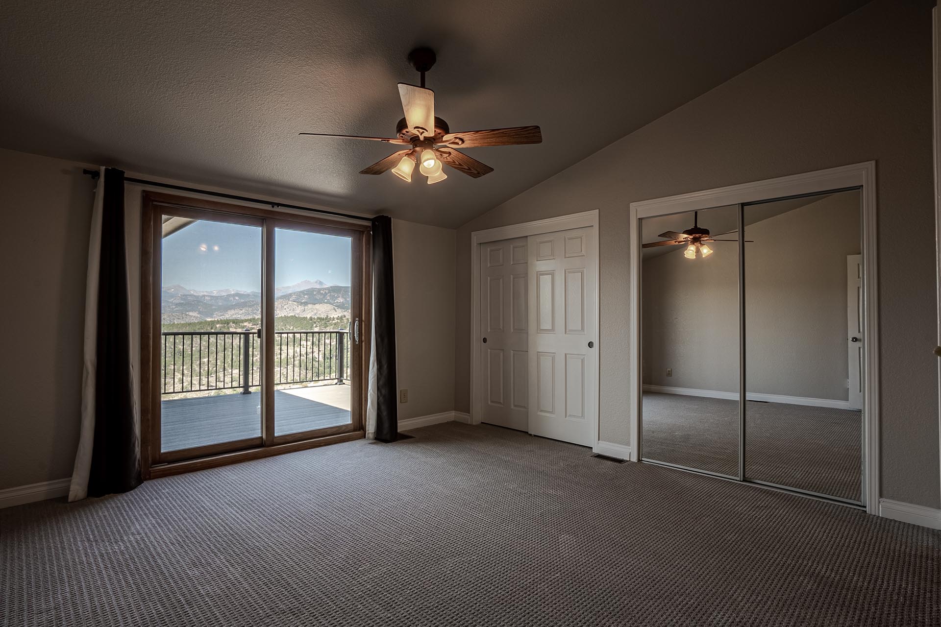 Bedroom with a ceiling fan and lights, sliding glass door to a balcony showing mountains outside, and a mirrored closet door.