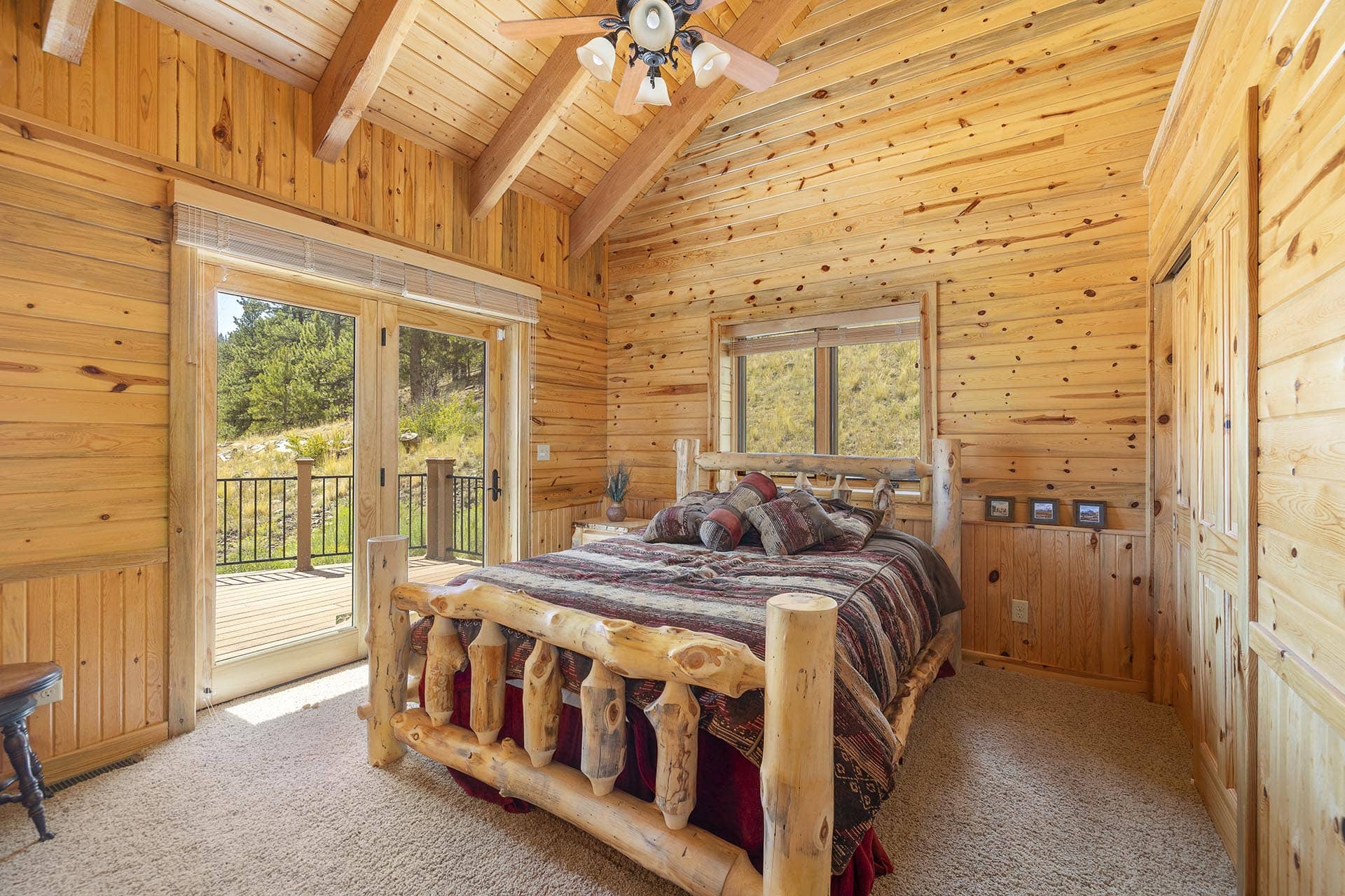 Cozy rustic bedroom in a log cabin with a carved wooden bed and large windows overlooking trees outside.