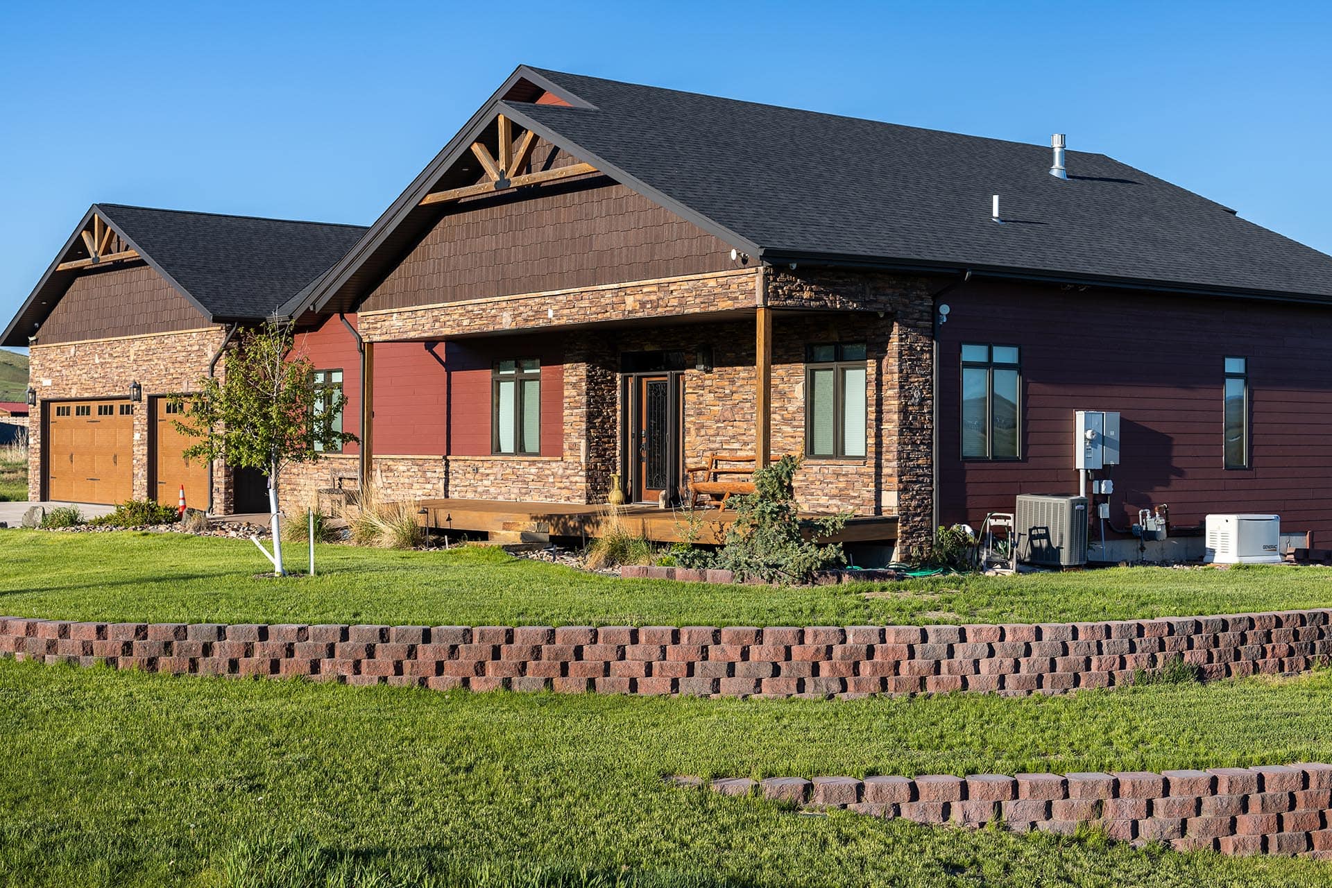 Front view of a modern ranch-style house with stone veneer, wood siding, and a front porch under a clear blue sky.