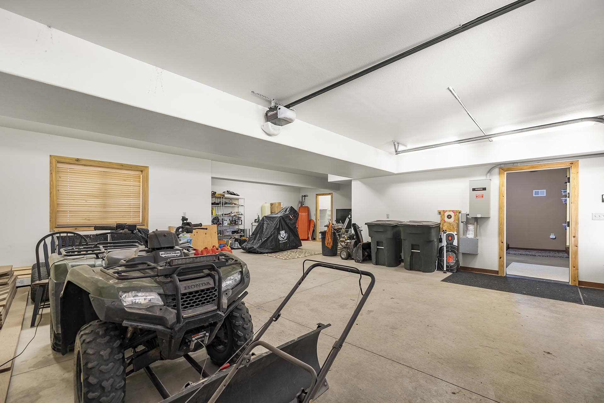 A cluttered garage with two all-terrain vehicles in the foreground and shelving, tools, and storage bins in the background.