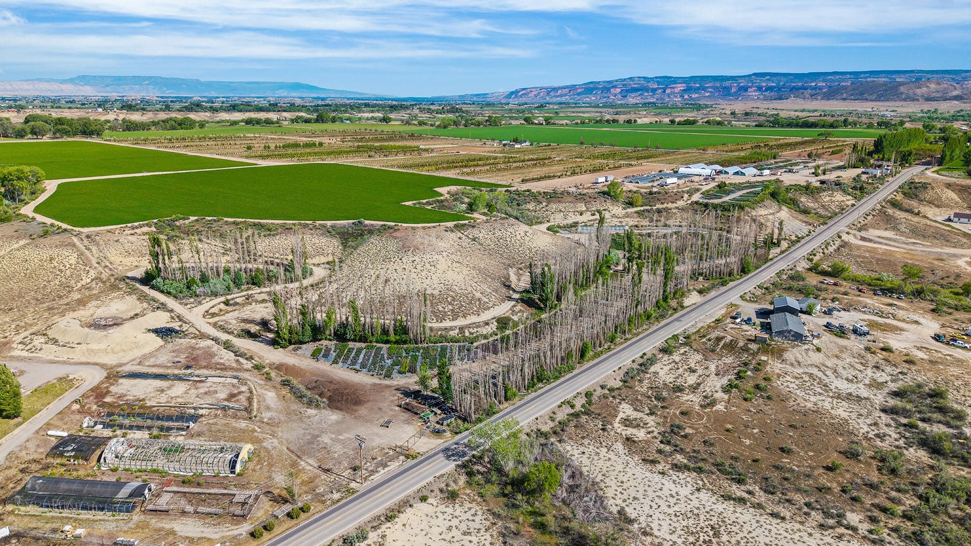 Aerial view of farmland with bright green fields, a main road cutting through, and distant hills on the horizon.