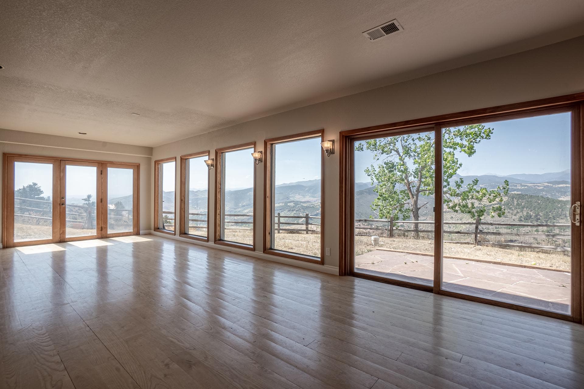 Sunlit living room with large floor-to-ceiling windows and sliding glass doors showing a hillside landscape outside.