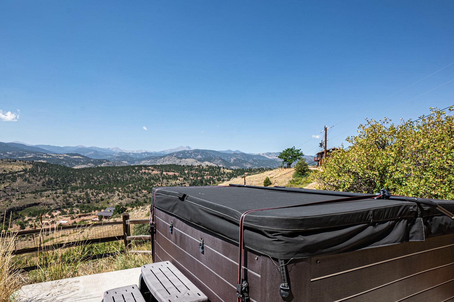 Brown camping trailer on a hillside with mountains in the distance and a clear blue sky in the background