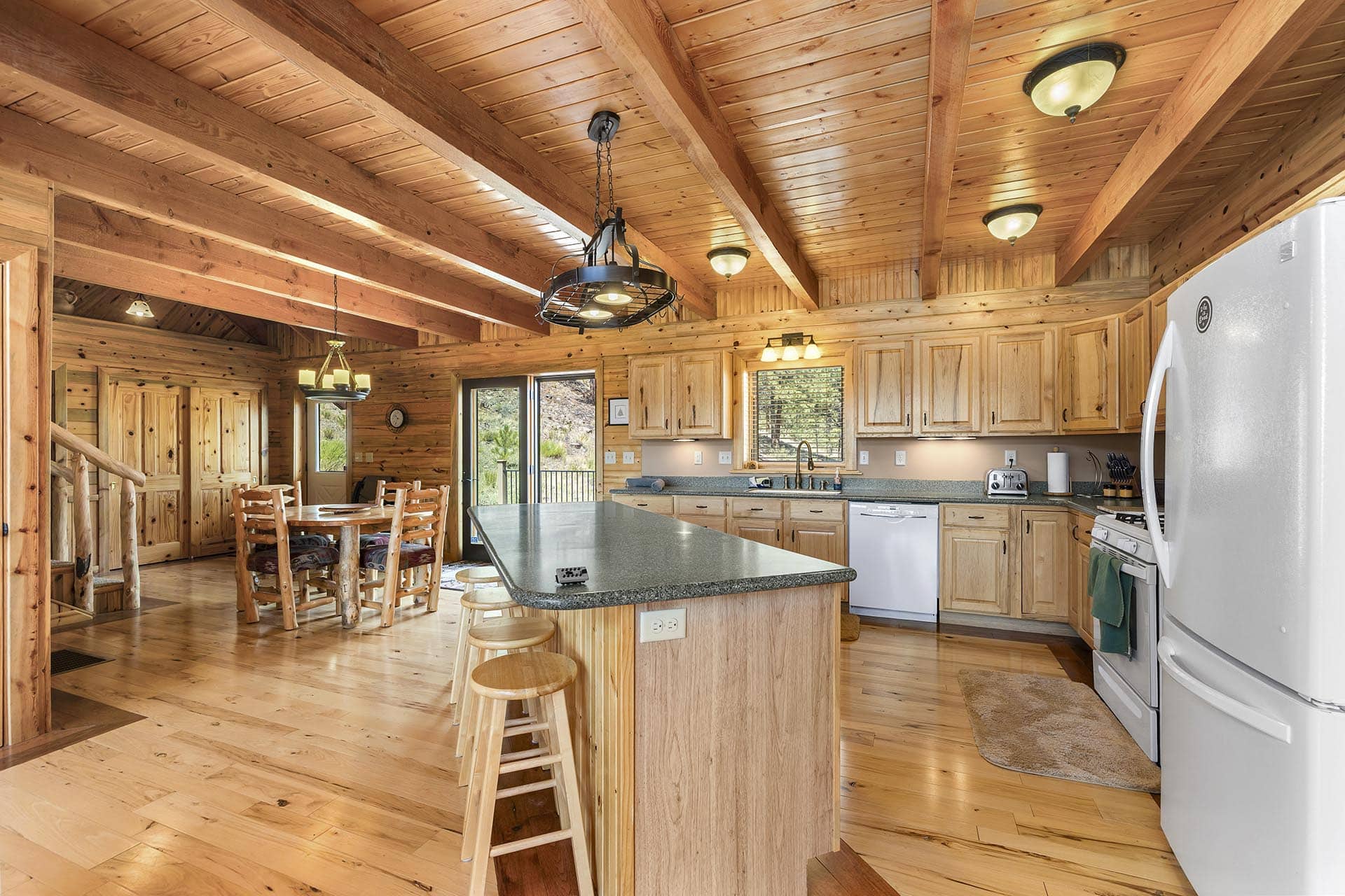 Rustic log-cabin kitchen with a large island, wooden cabinets, and exposed ceiling beams.