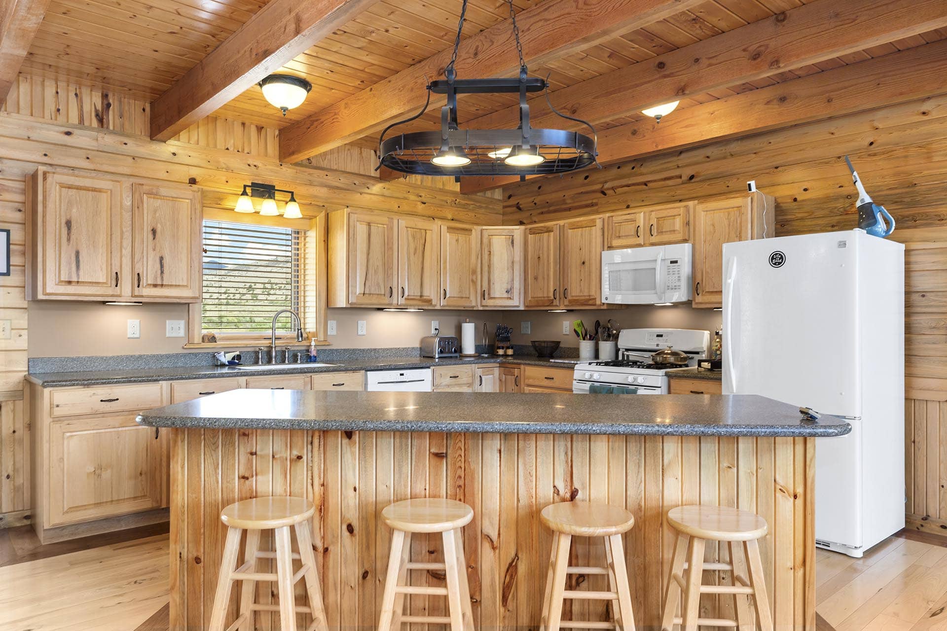 Rustic kitchen with wooden log cabin-style cabinets, a granite island, and a hanging circular chandelier.