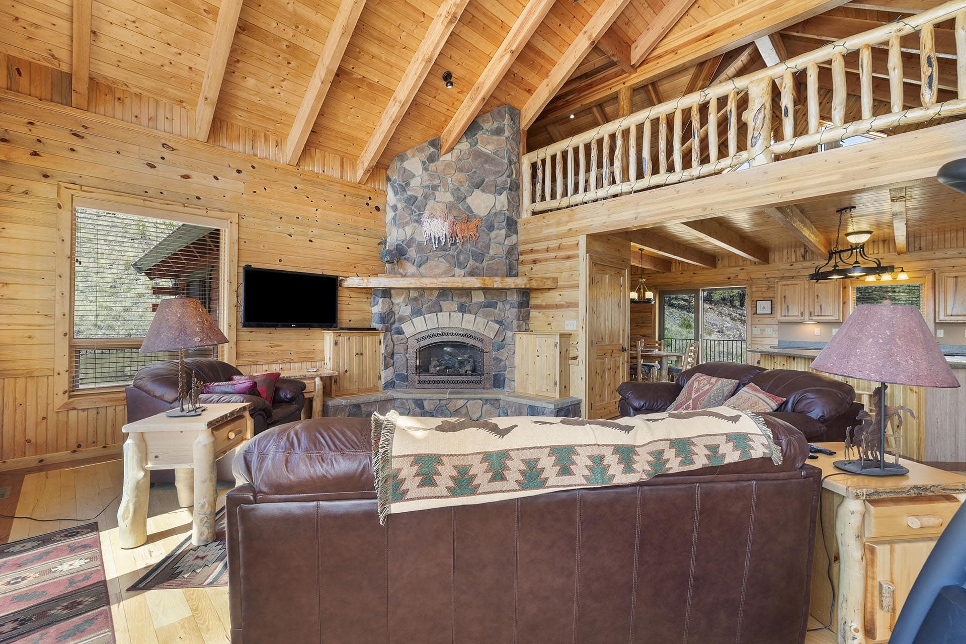 Cozy log cabin living room with a stone fireplace, leather sofas, and rustic wooden beams.