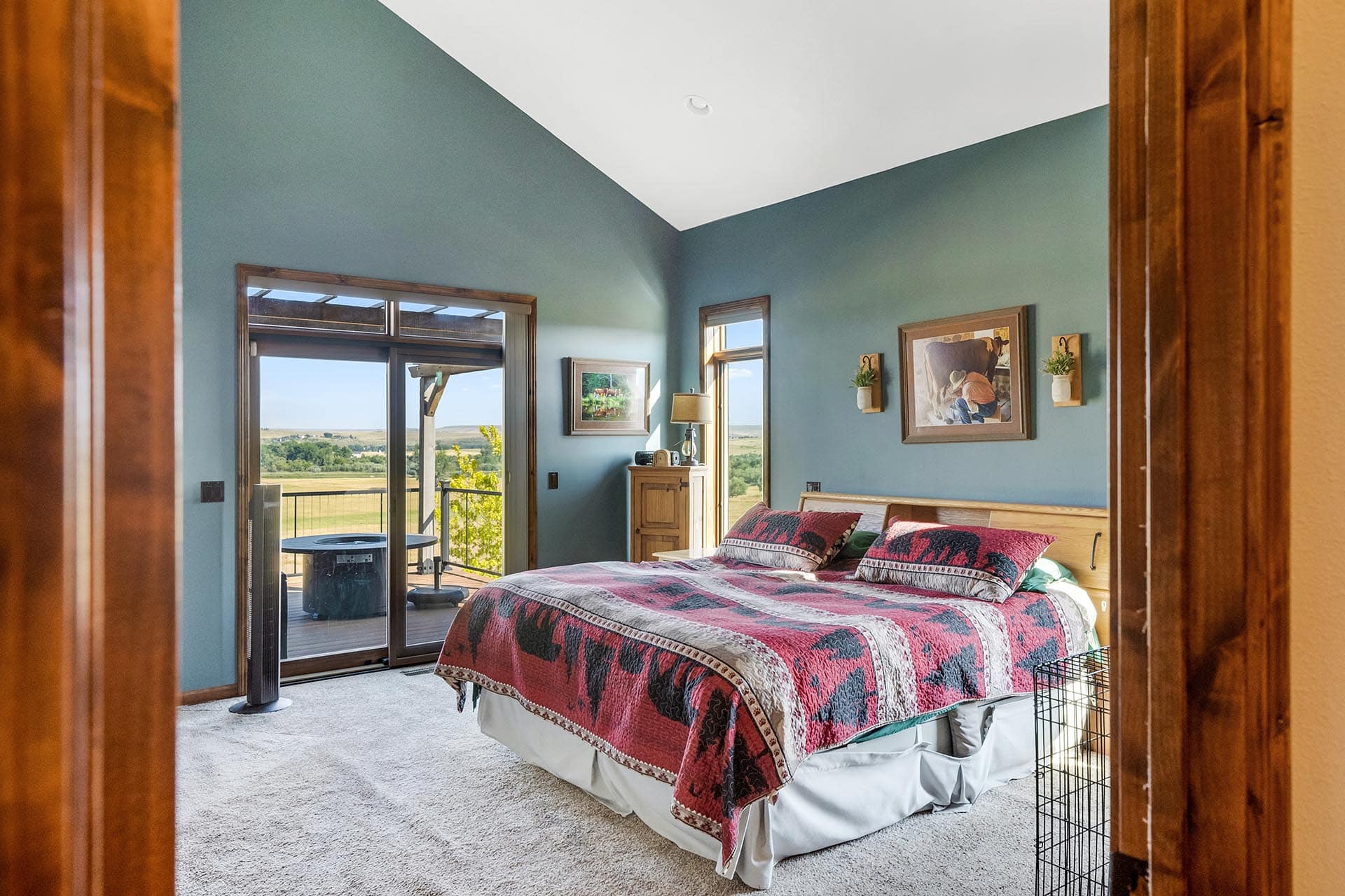 Bedroom with teal walls, a wooden bed and dresser, and a red patterned quilt; sliding glass door to a deck with countryside view