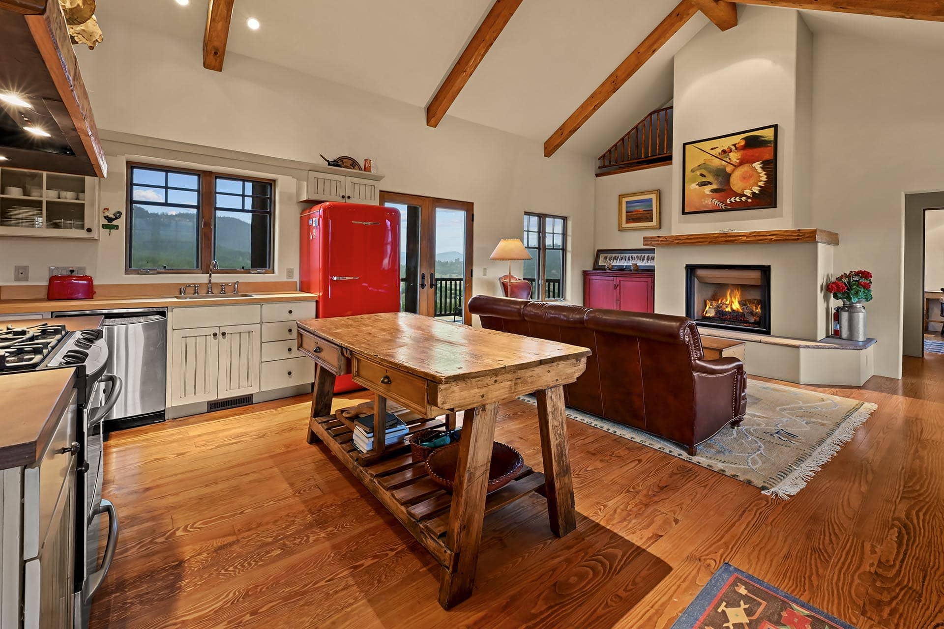 Open-plan kitchen and living room with exposed wooden ceiling beams, a bright red vintage refrigerator, and a fireplace.