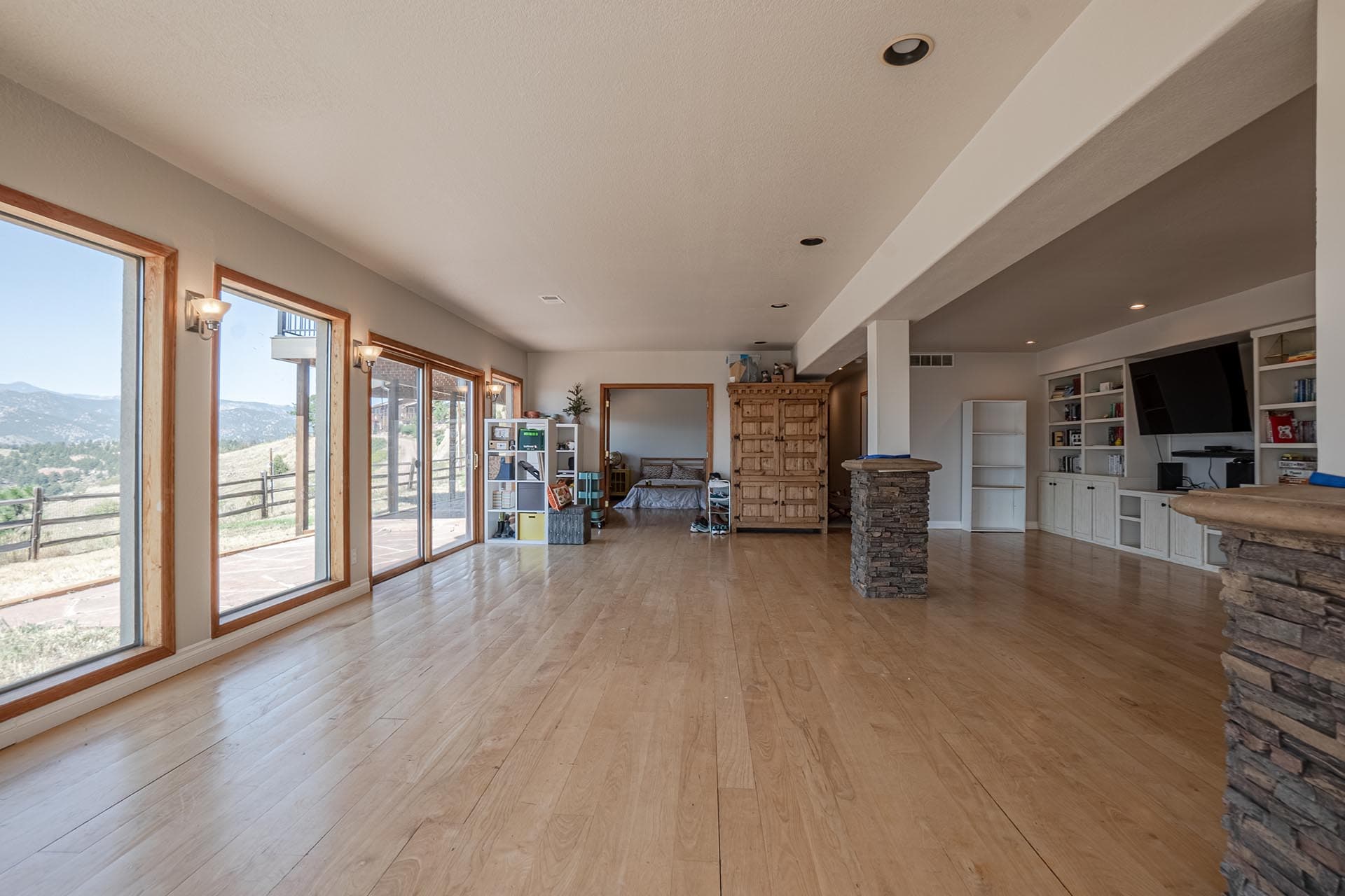 Open living area with wide sliding glass doors to a hillside landscape, light wood floors, and built-in shelves along the right wall.